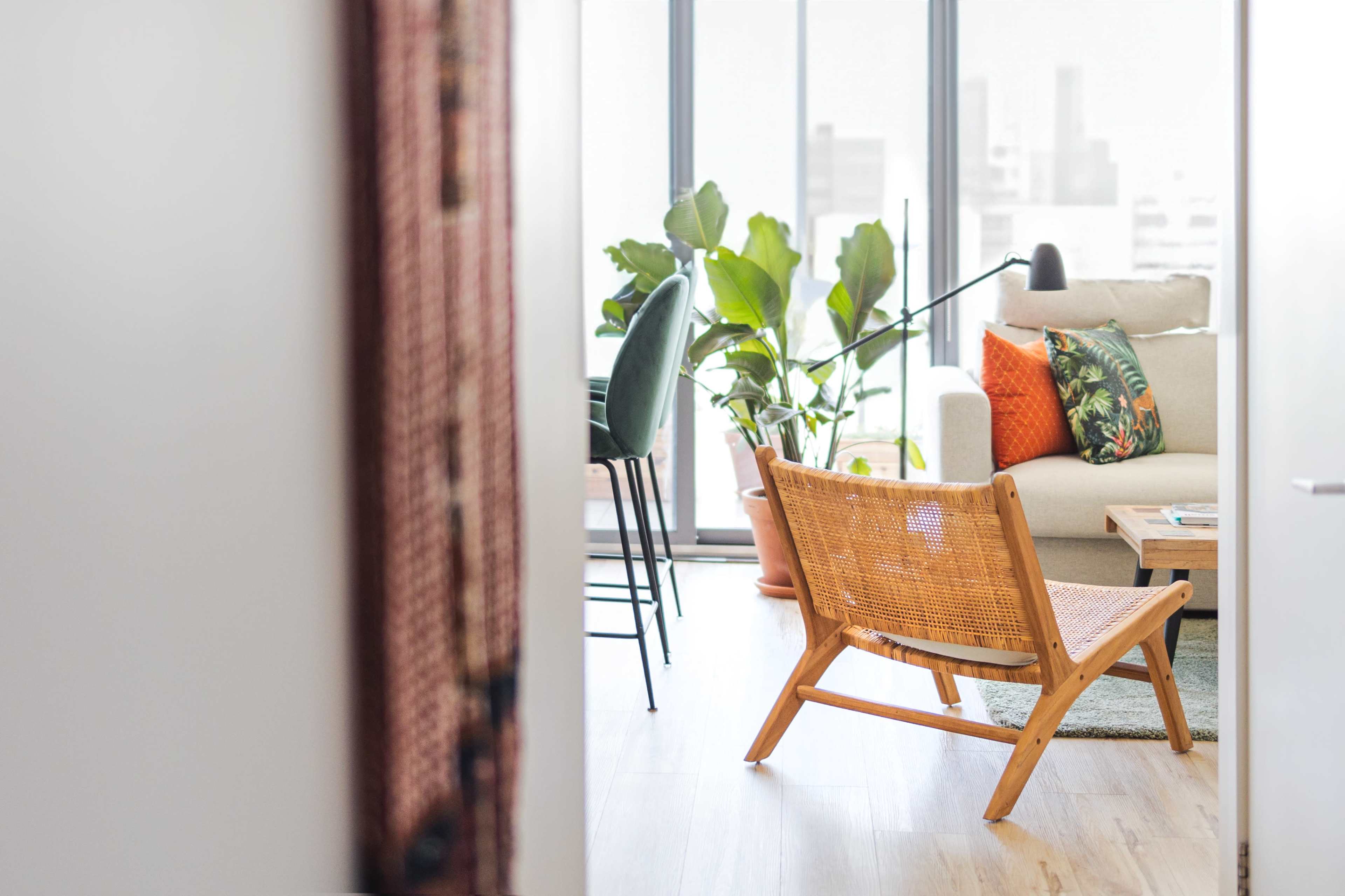 A wooden chair faces a living room with a sofa, a coffee table, and large windows overlooking city buildings.