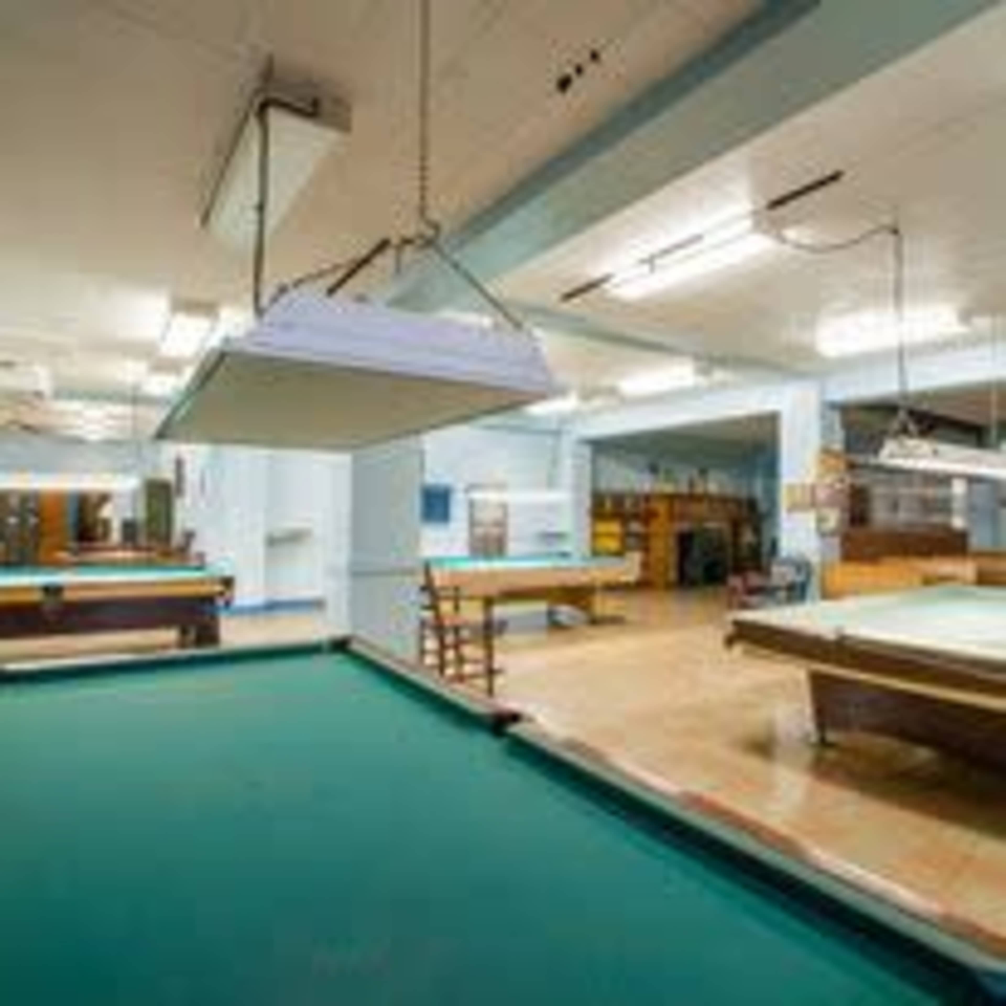 An interior of a game room with multiple pool tables and overhead lighting.