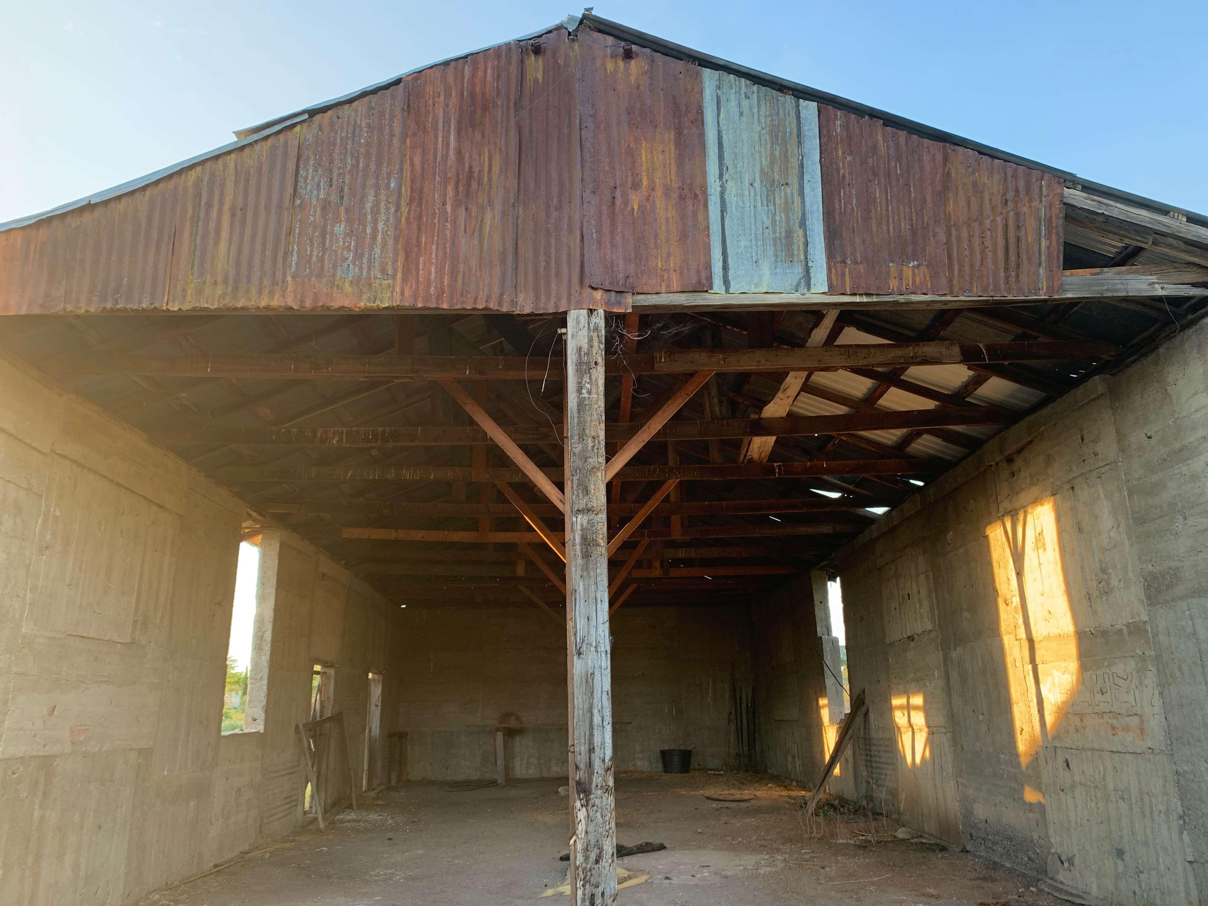 The image shows the interior of an old, weathered barn with a metal roof and exposed wooden beams.