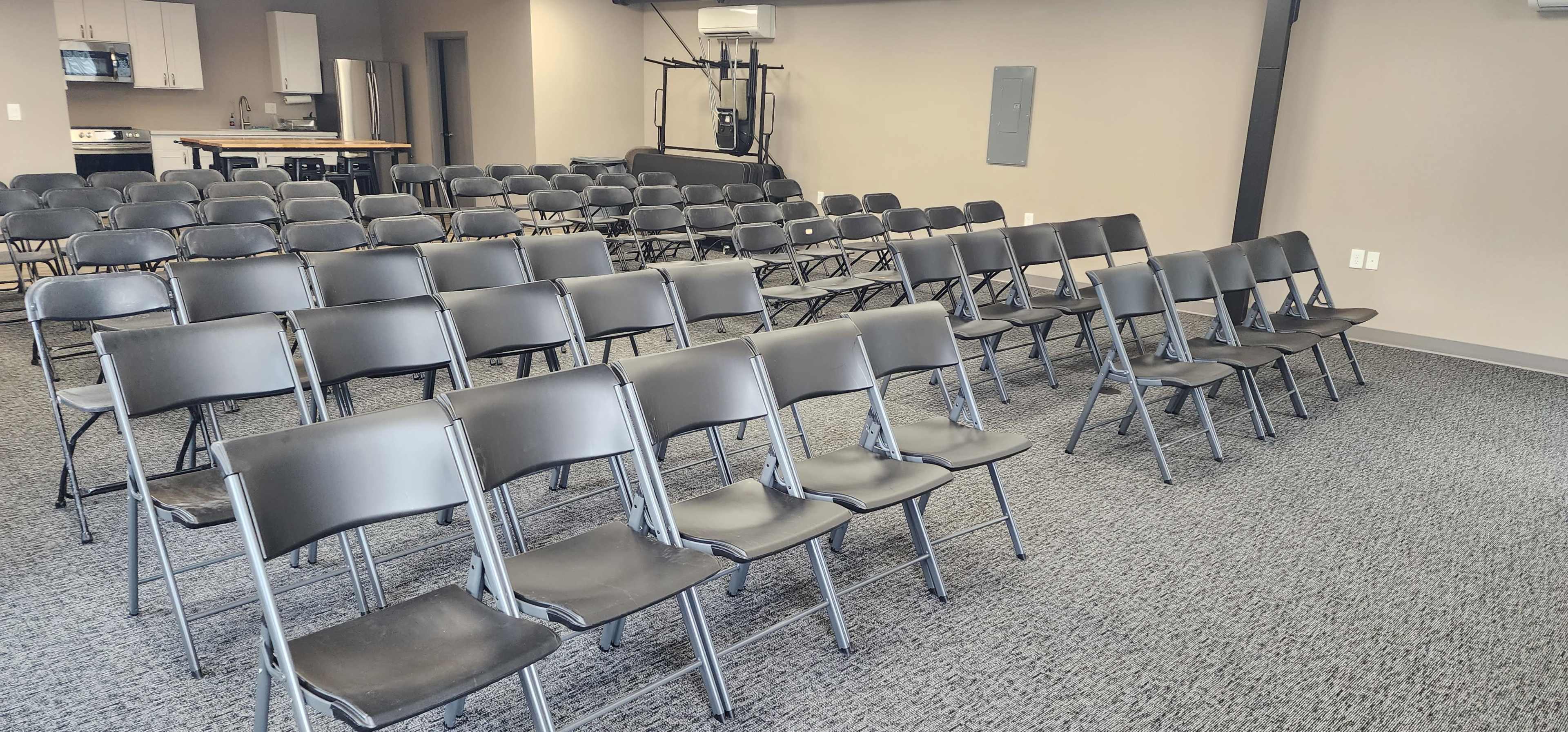 A spacious room arranged with multiple rows of metal folding chairs facing a central area.