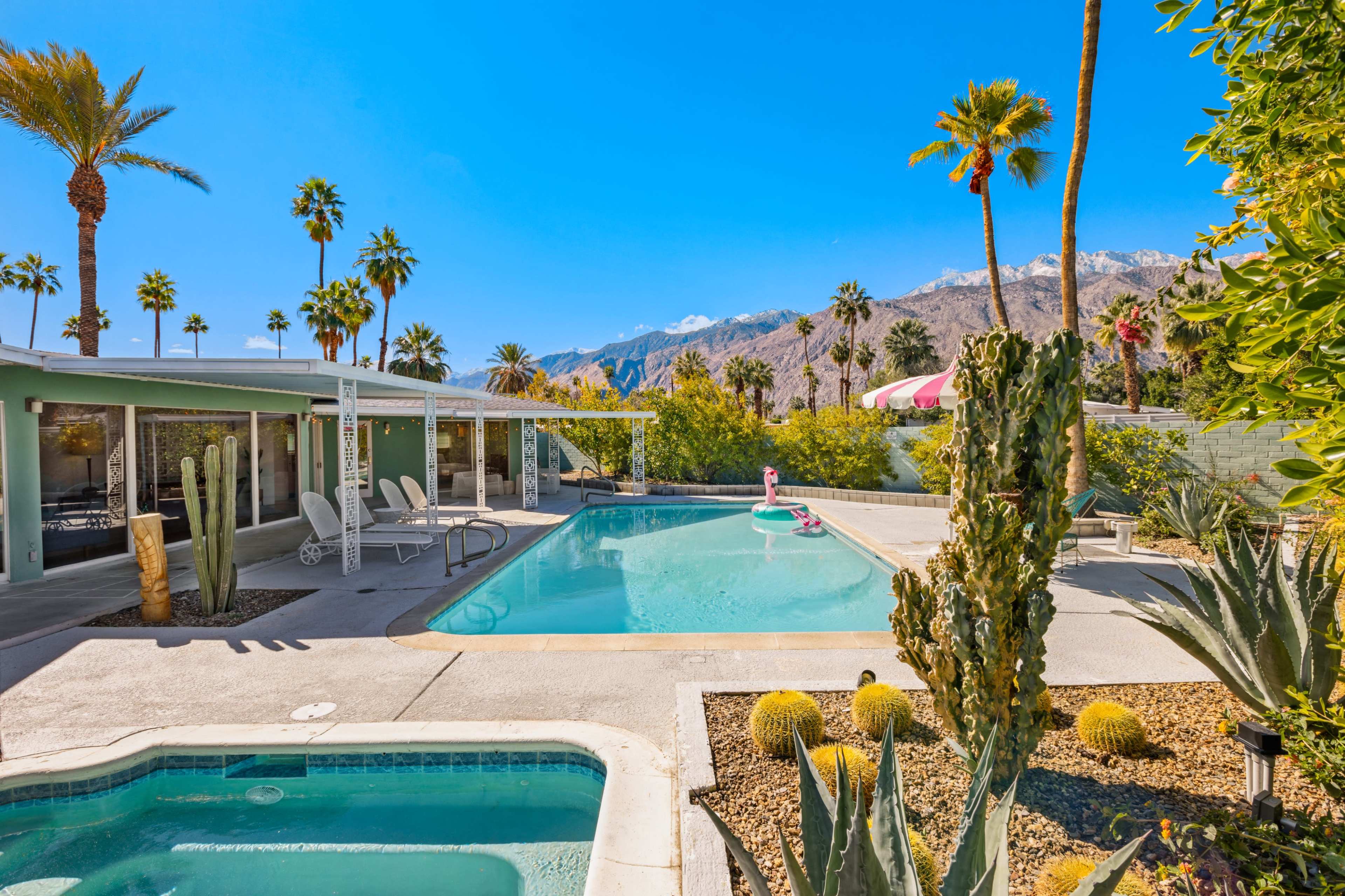 A swimming pool surrounded by palm trees and desert landscaping with mountains in the background.
