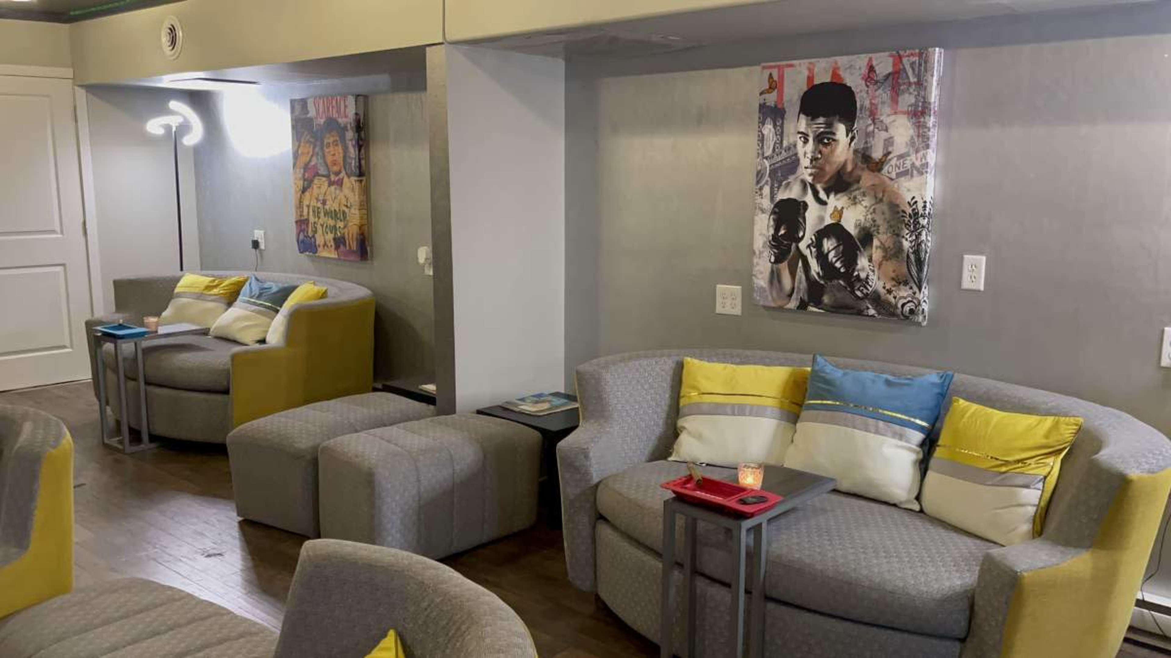 The image shows a modern seating area featuring curved couches with colorful cushions, small side tables, and artwork on the walls.