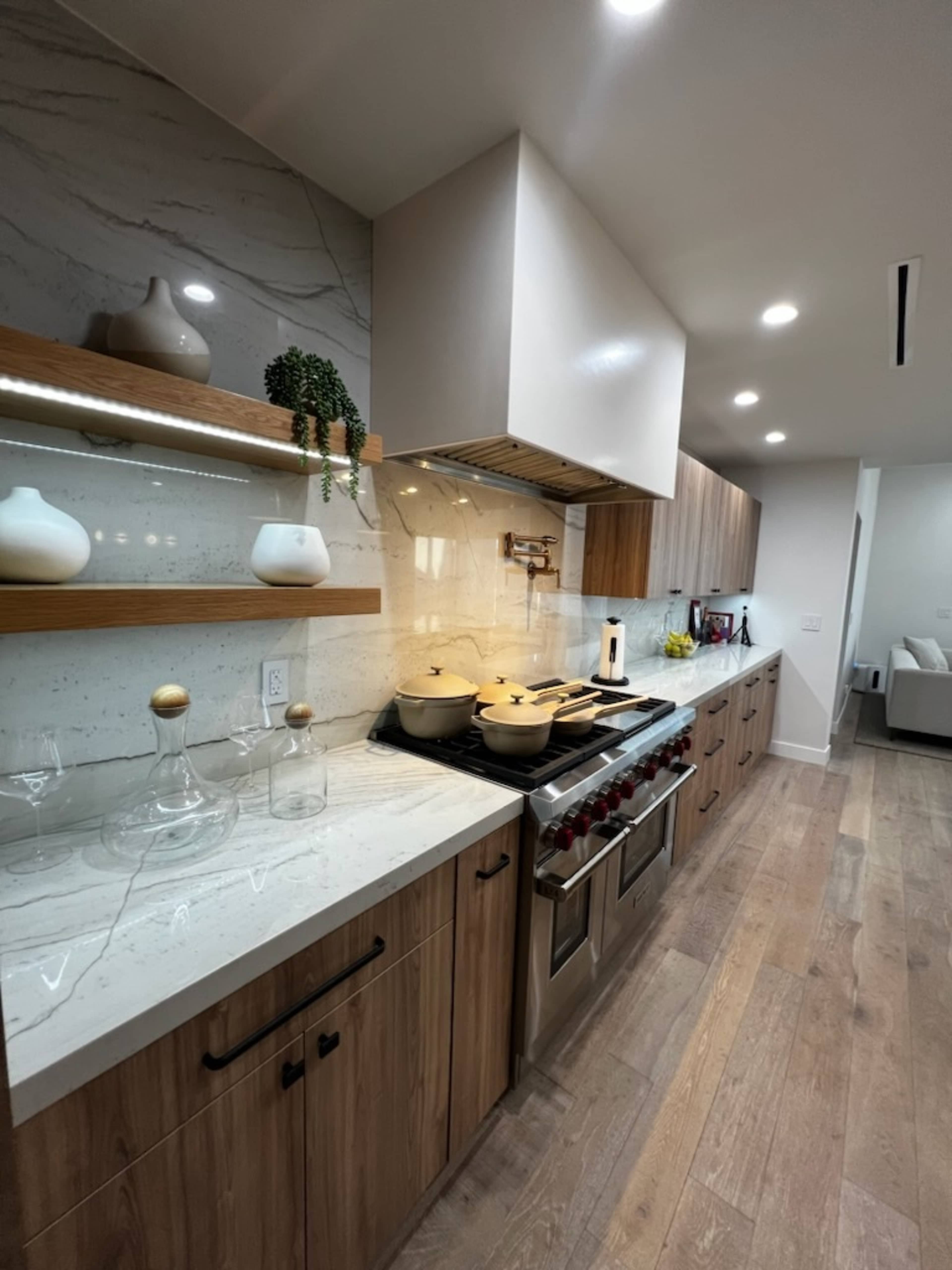 A modern kitchen featuring wood and stone cabinetry, a stainless steel gas range, and decorative glassware on the countertop.