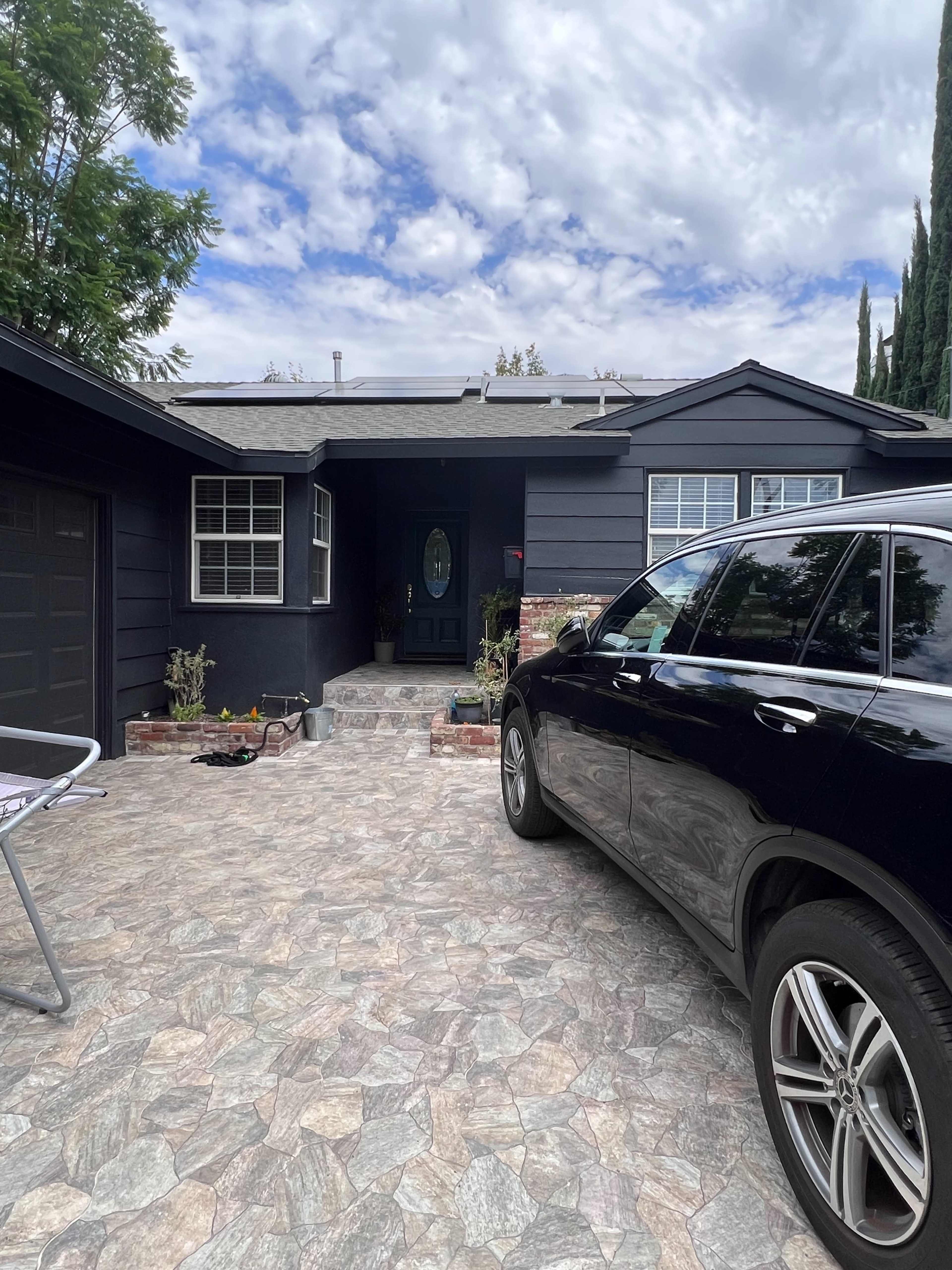 A black car is parked in the driveway of a dark-colored house with a stone pathway leading to the front door.