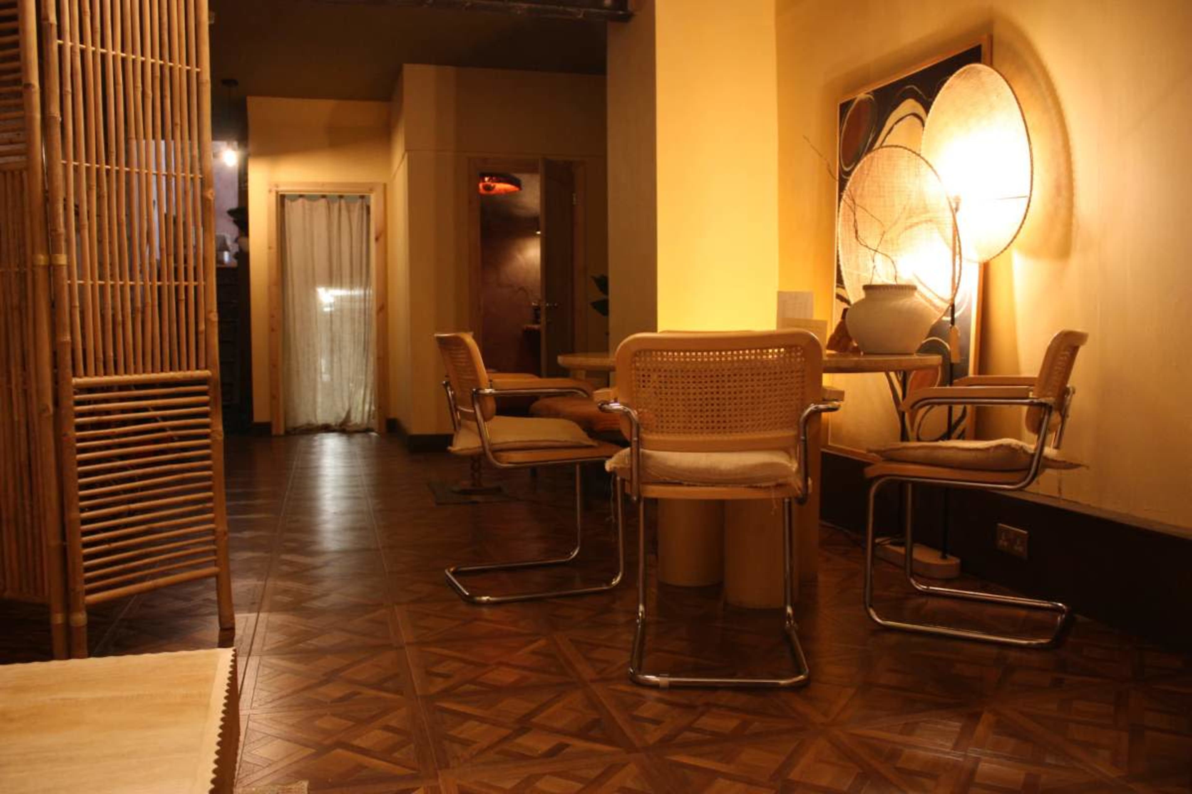 A dimly lit interior space featuring a small dining area with four chairs and a table, surrounded by wooden partitions and warm-toned decor.