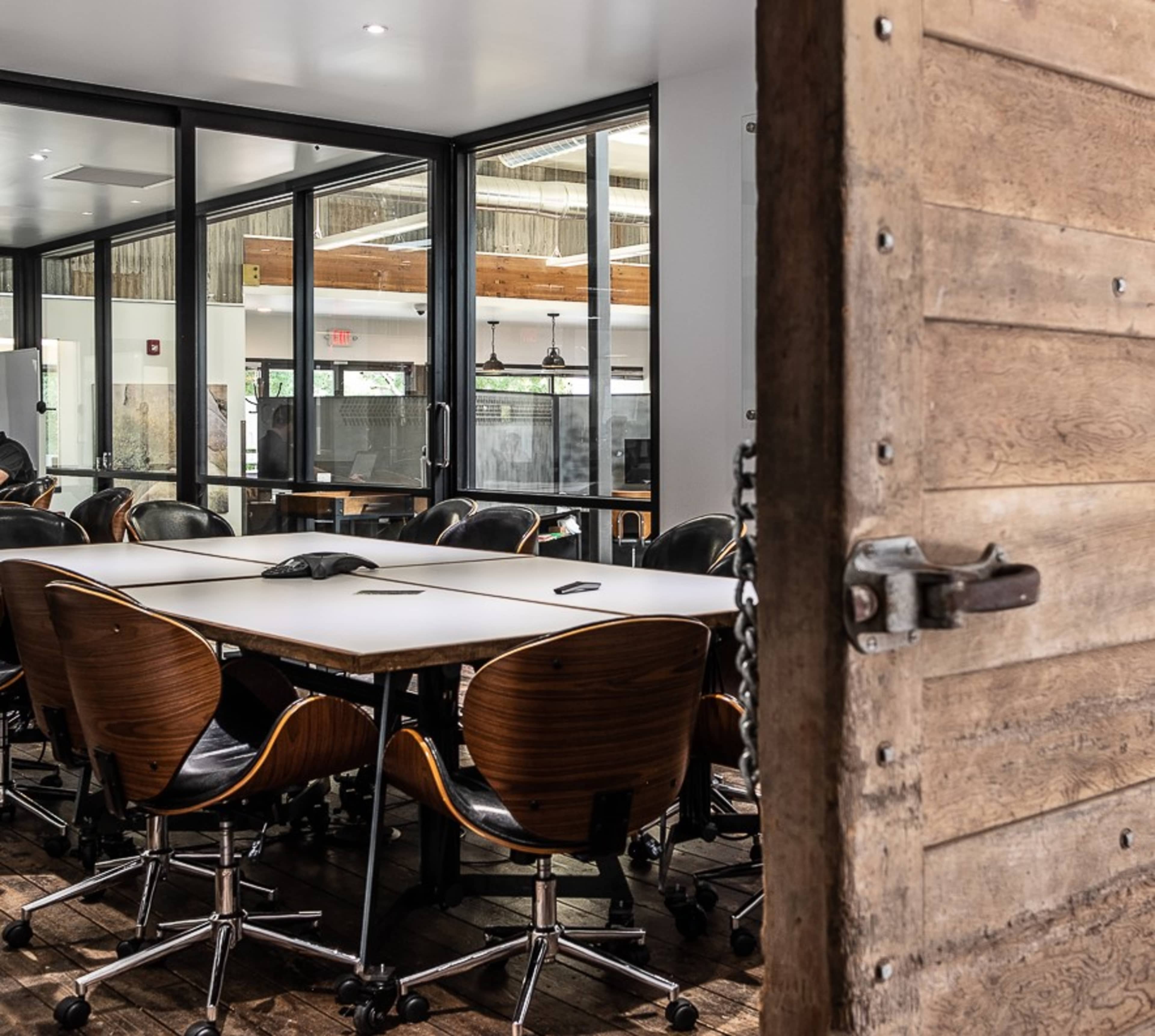 A conference room with a large table surrounded by ergonomic chairs and a wooden door partially open.