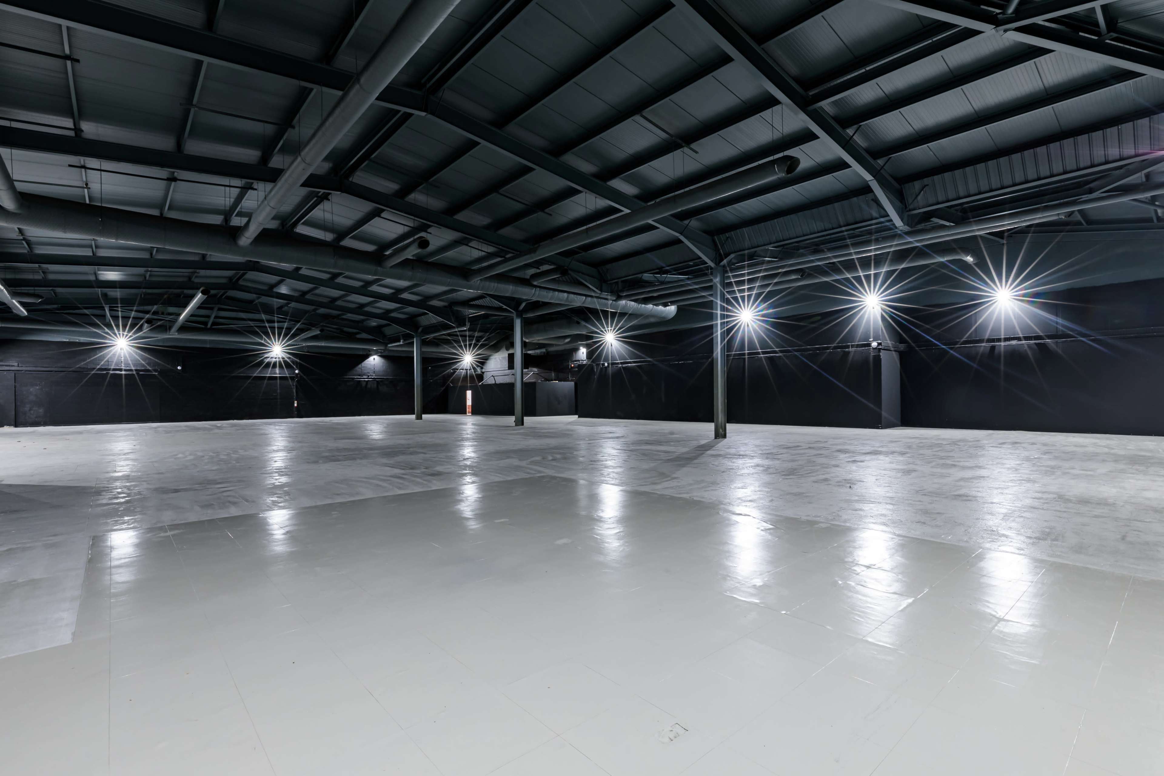 The image shows a large, empty industrial space with a high ceiling and bright overhead lights illuminating the floor.