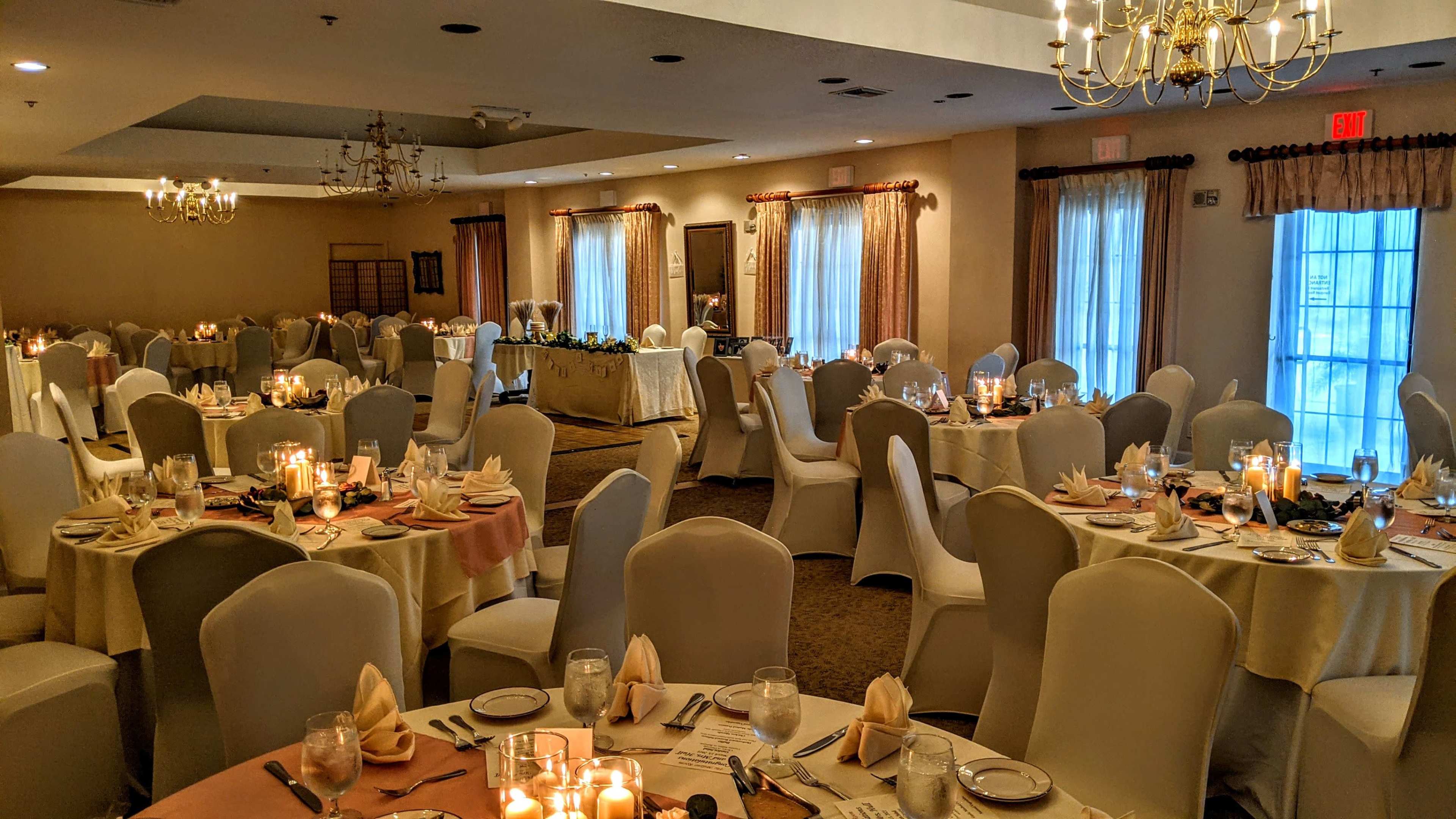 A banquet hall set up for an event, featuring neatly arranged tables with white tablecloths, candles, and place settings.