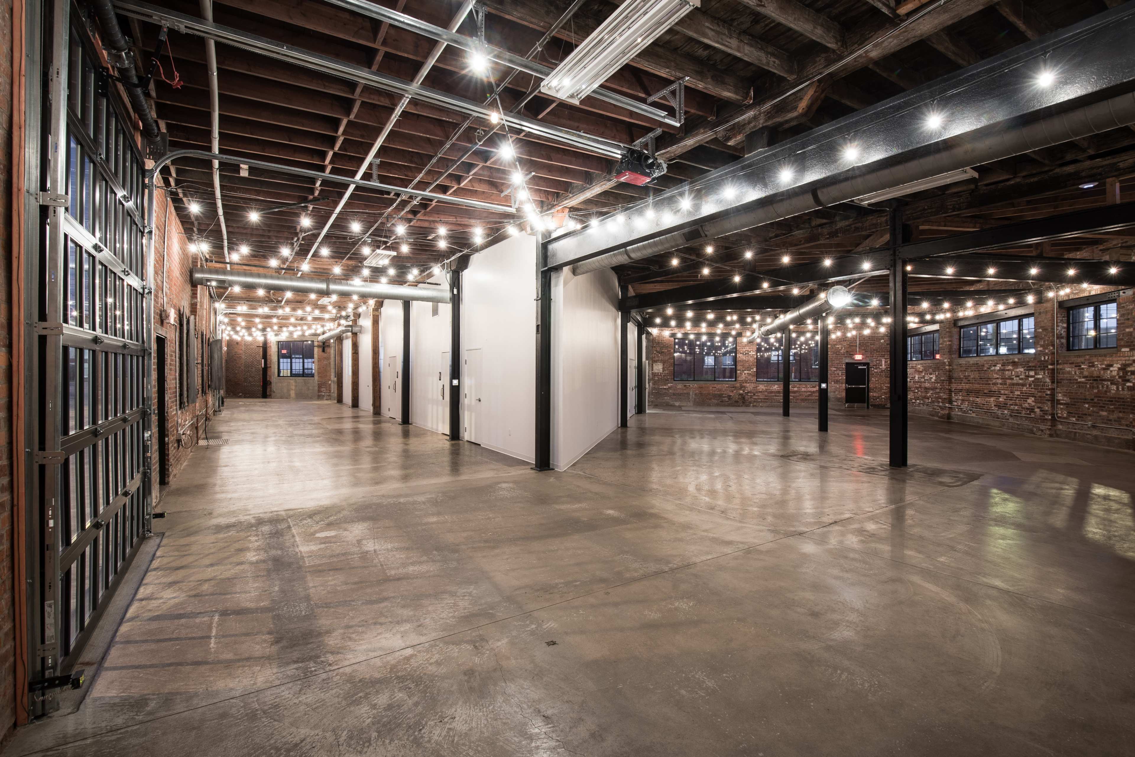 An industrial-style event space with exposed brick walls, high ceilings, and string lights illuminating the area.