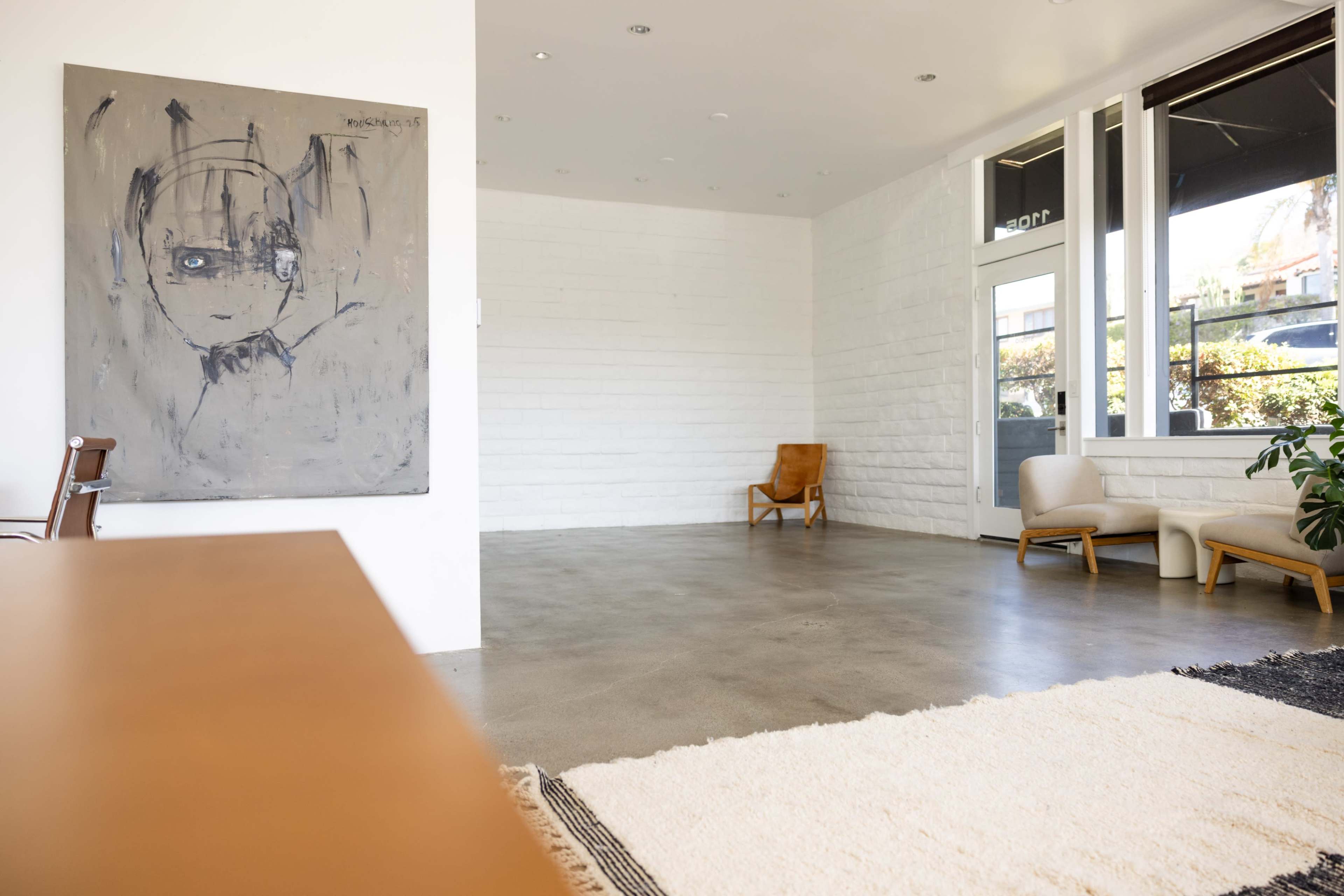 The image depicts an empty modern interior space featuring a large abstract painting on one wall, two seating chairs, and a concrete floor.