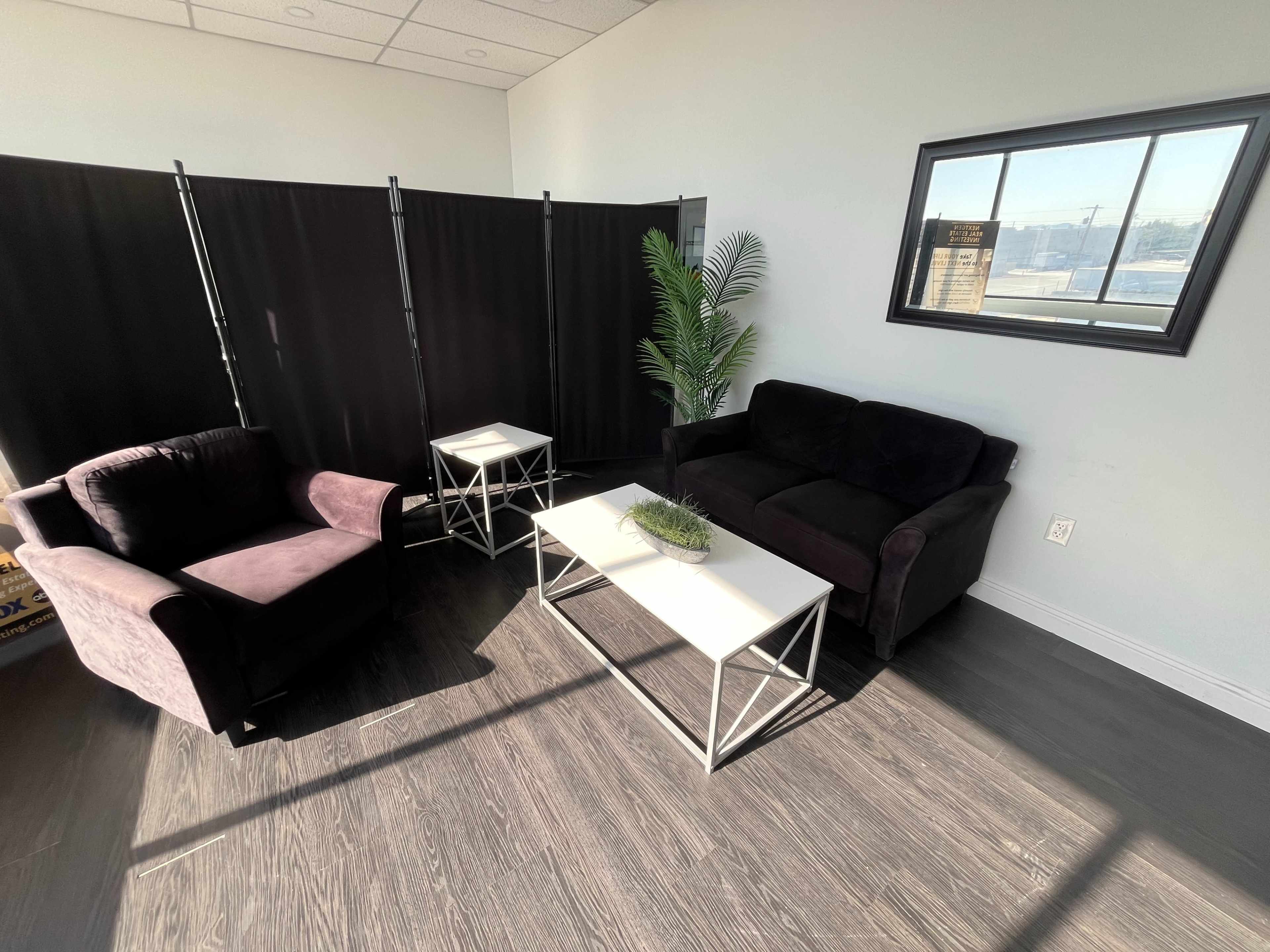 A dark seating area features a purple armchair and a black sofa, paired with two white tables and a black privacy divider in the background.