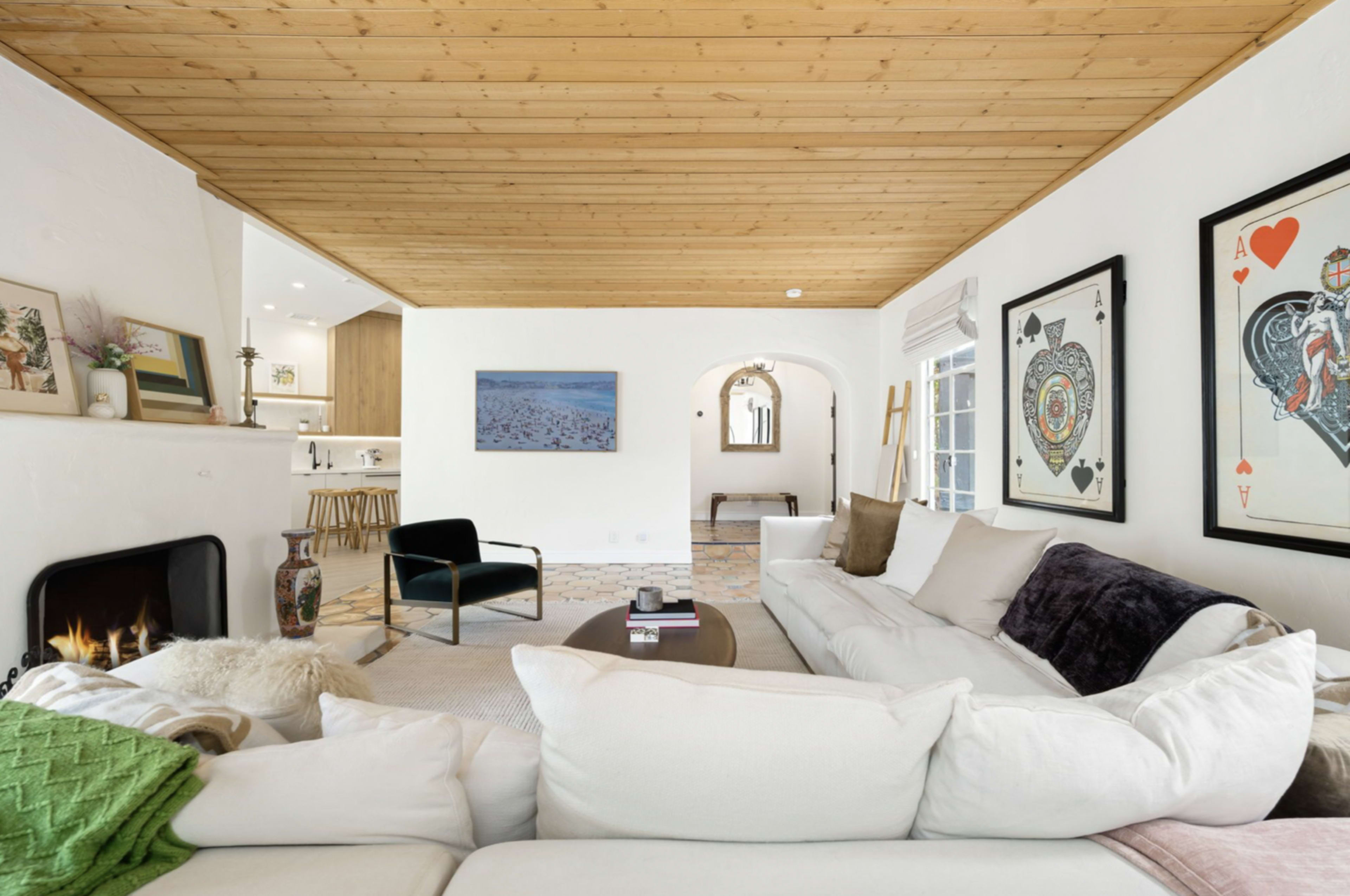 A bright living room with a white sectional sofa, wooden ceiling beams, and artwork featuring playing cards on the walls.