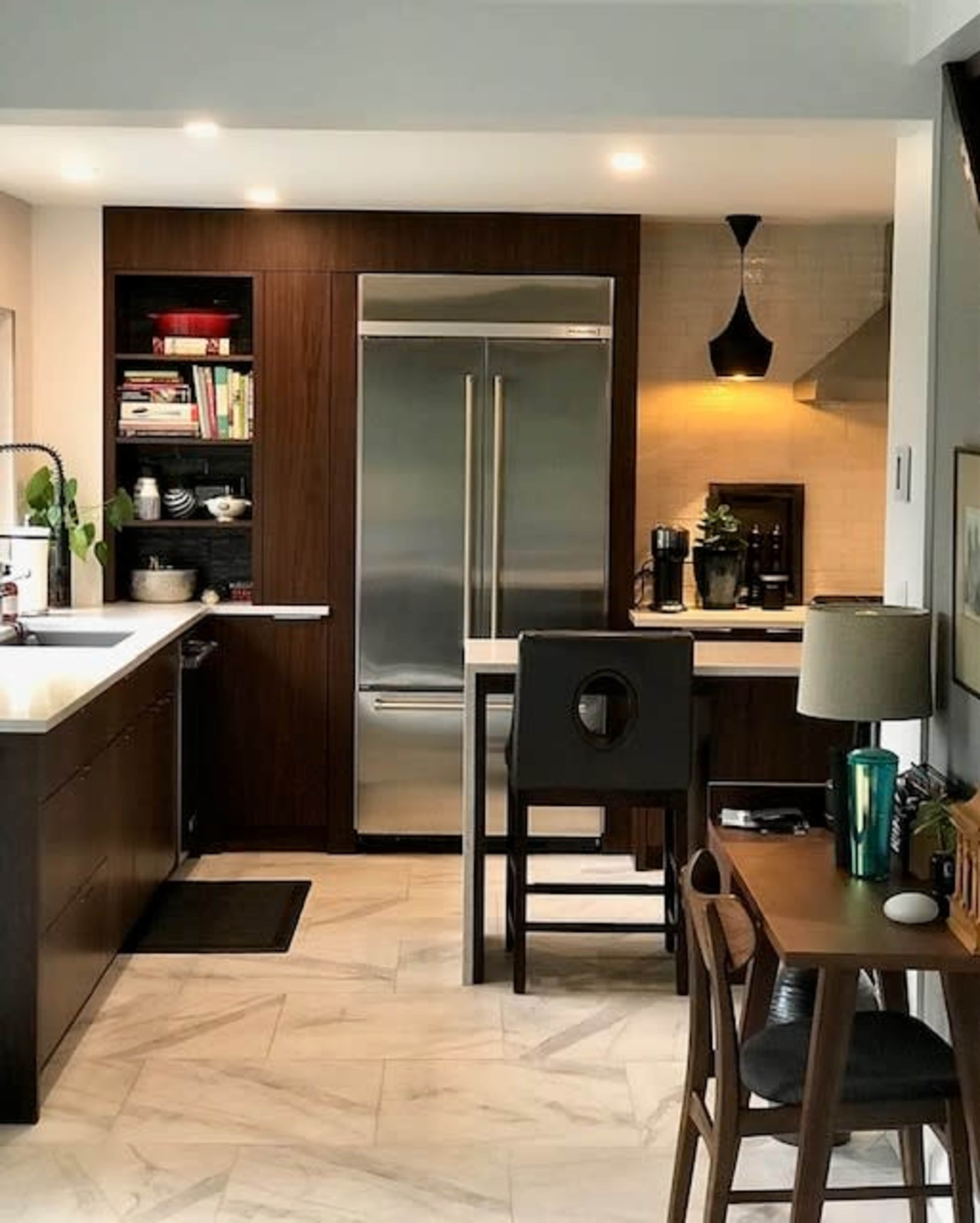 A modern kitchen features dark wood cabinetry, a stainless steel refrigerator, and a small dining area with a wooden table and chairs.