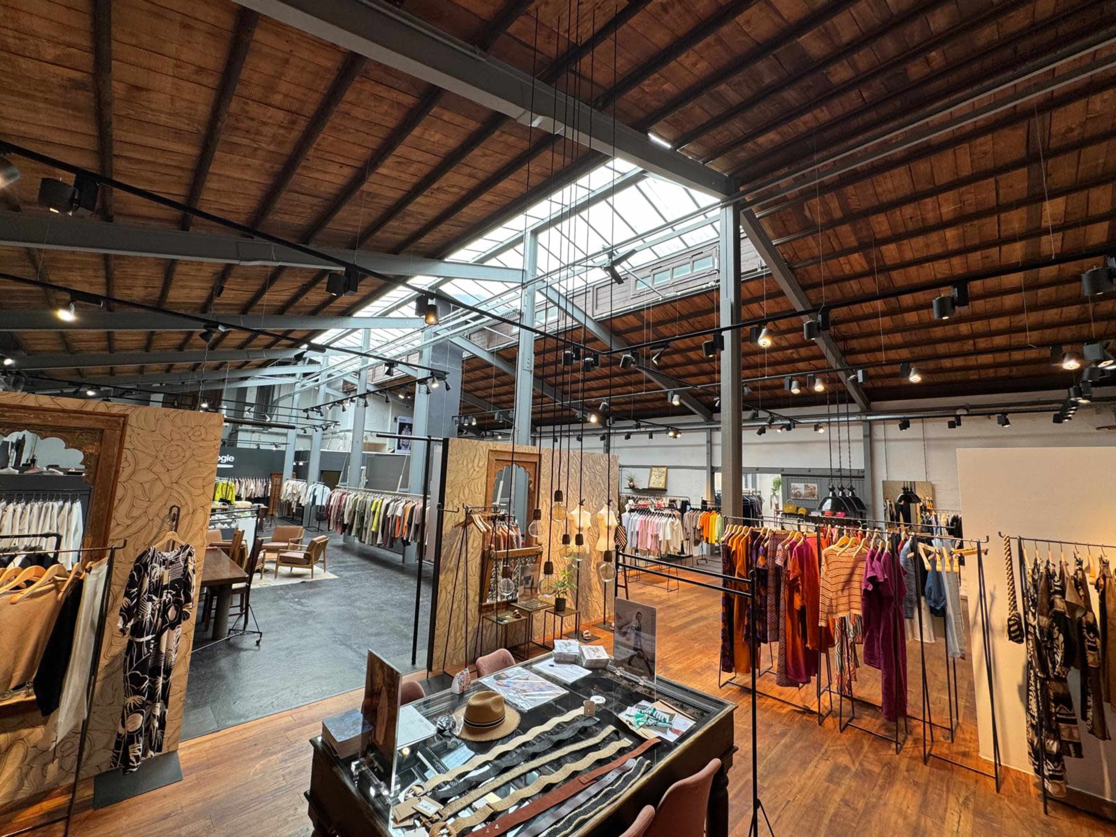The image shows a spacious retail clothing store with wooden beams and various clothing racks displaying a range of apparel.