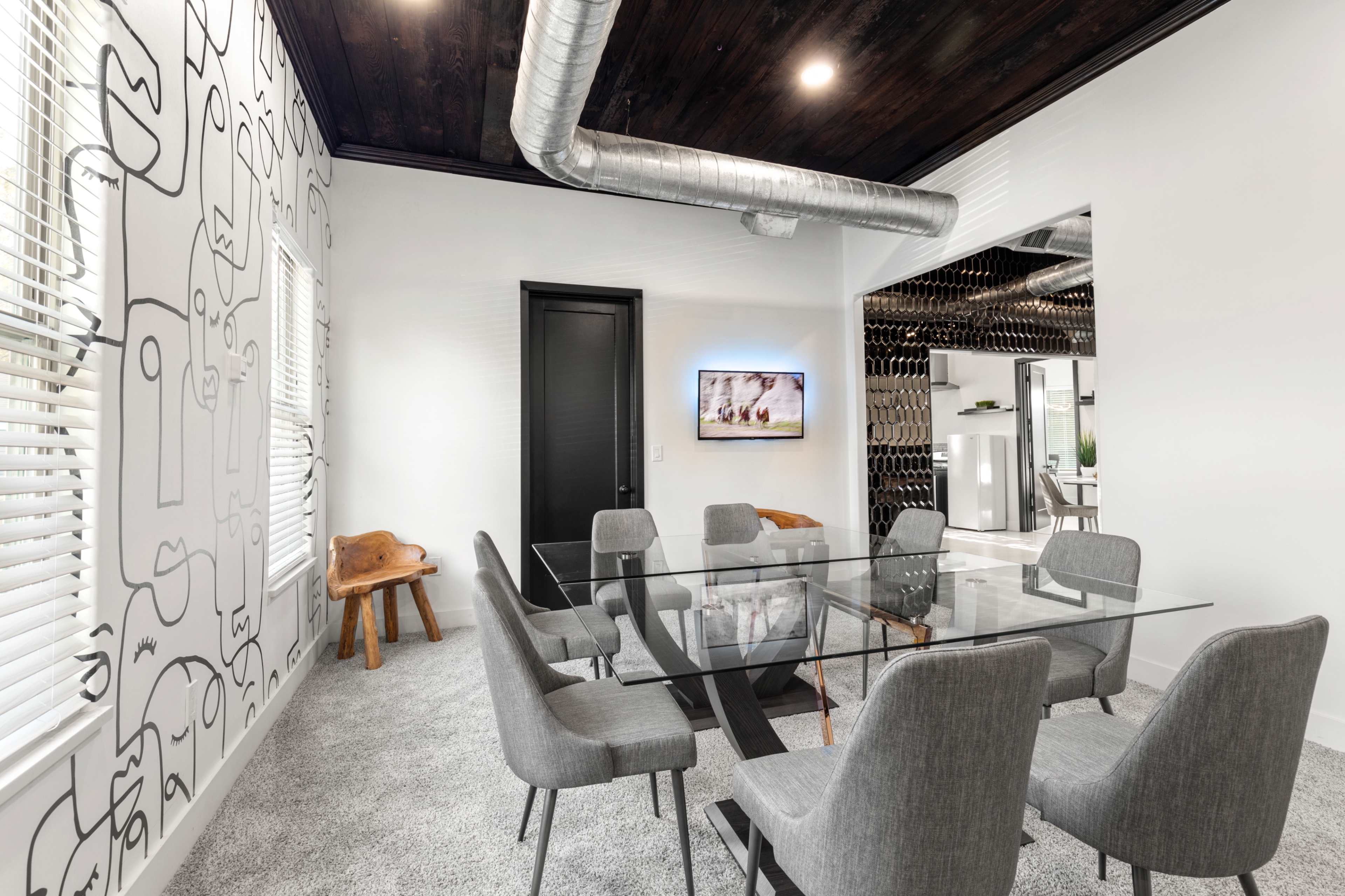 A modern conference room features a glass table surrounded by gray chairs, with a wall adorned with abstract line art and a TV mounted in the corner.