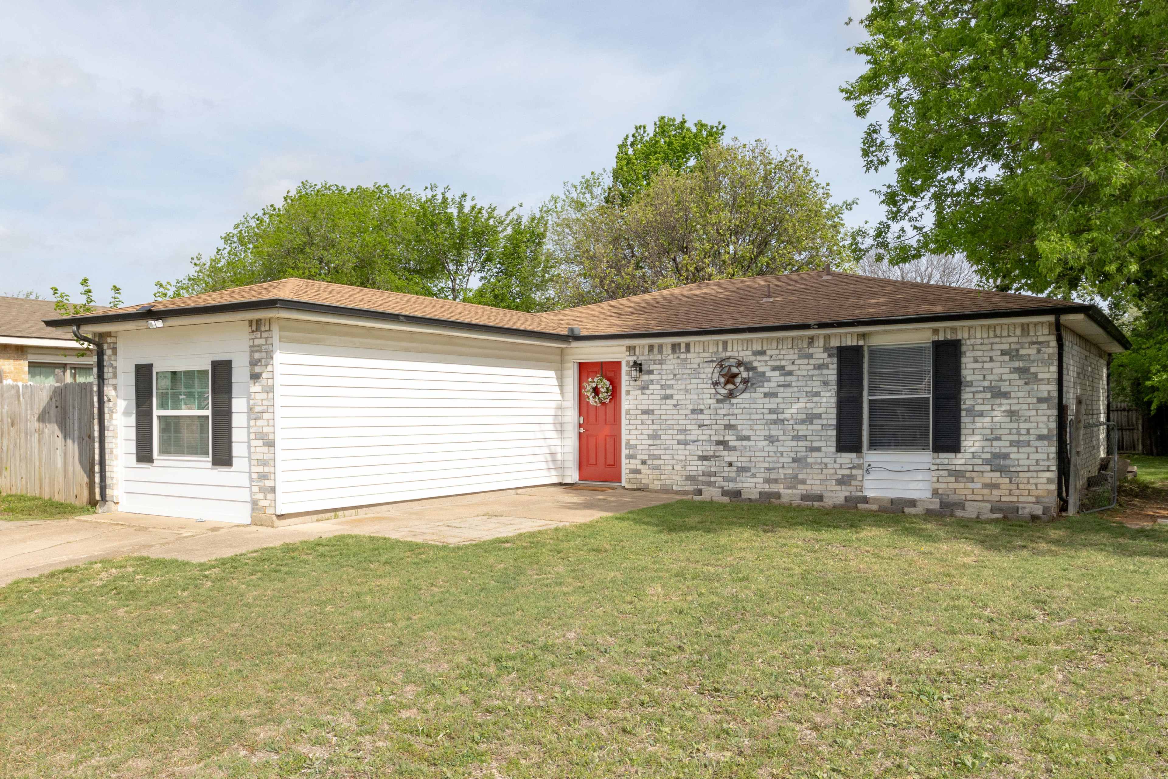 The image shows a single-story house with a brick exterior, a red front door, and a well-maintained lawn.