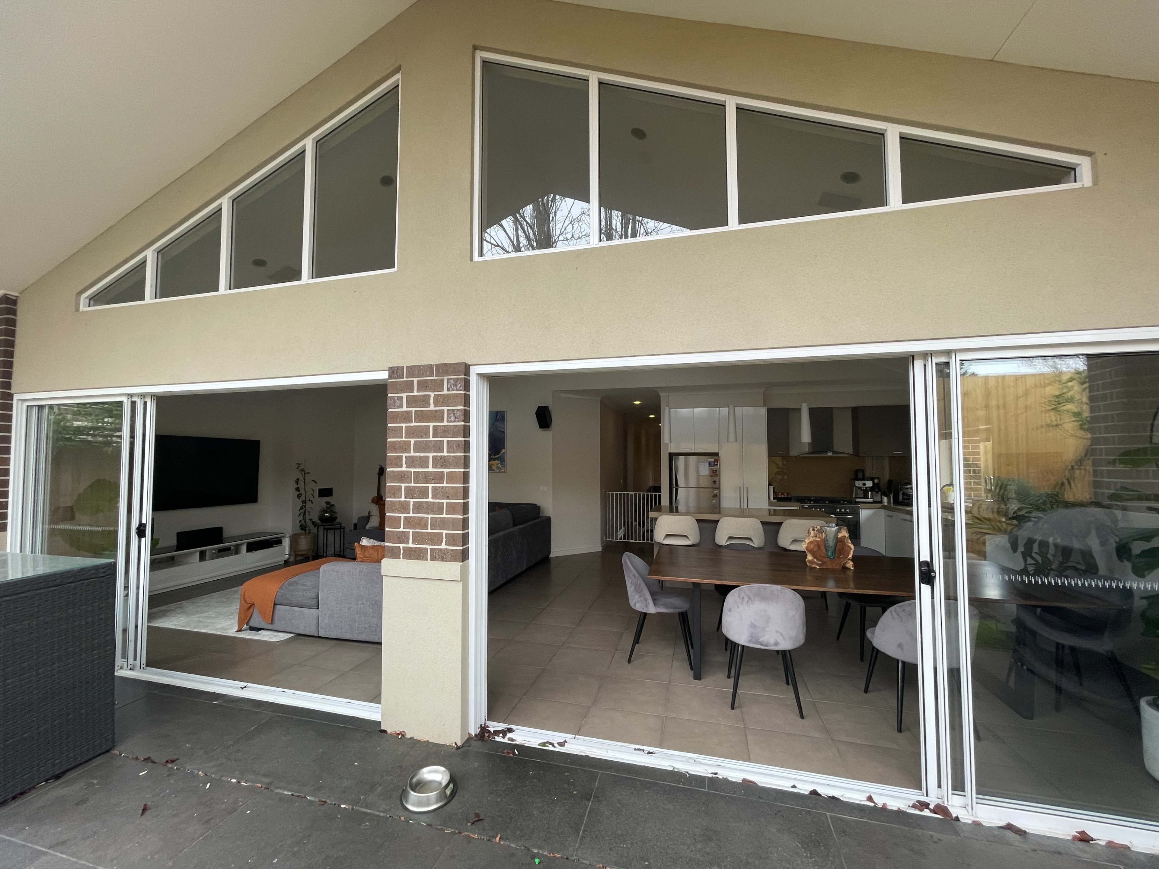 A spacious living area with large windows overlooks a dining table set for six, connecting an interior kitchen space to an outdoor patio.