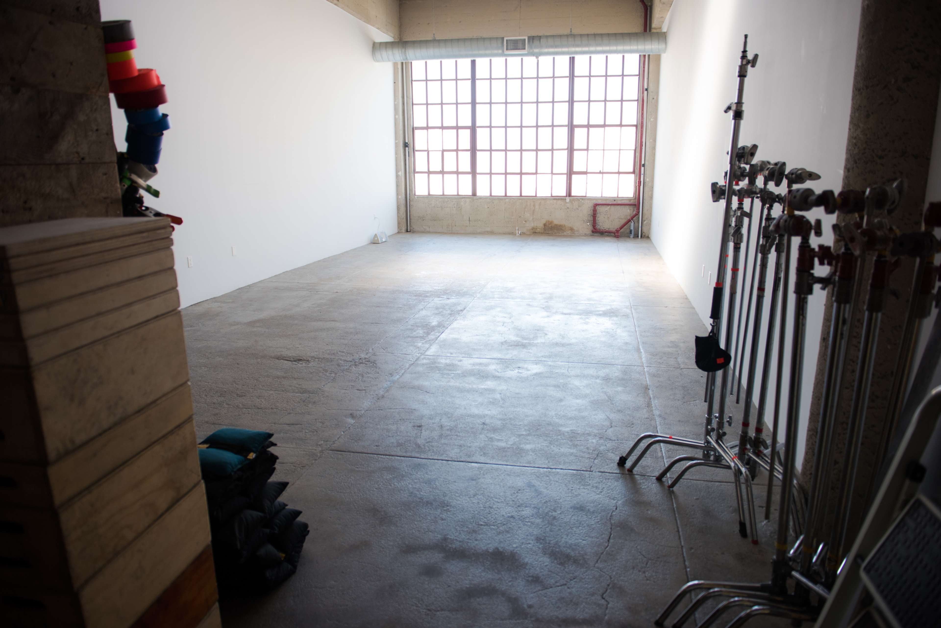An empty room with concrete flooring, large windows on one wall, and metal equipment arranged neatly along another wall.