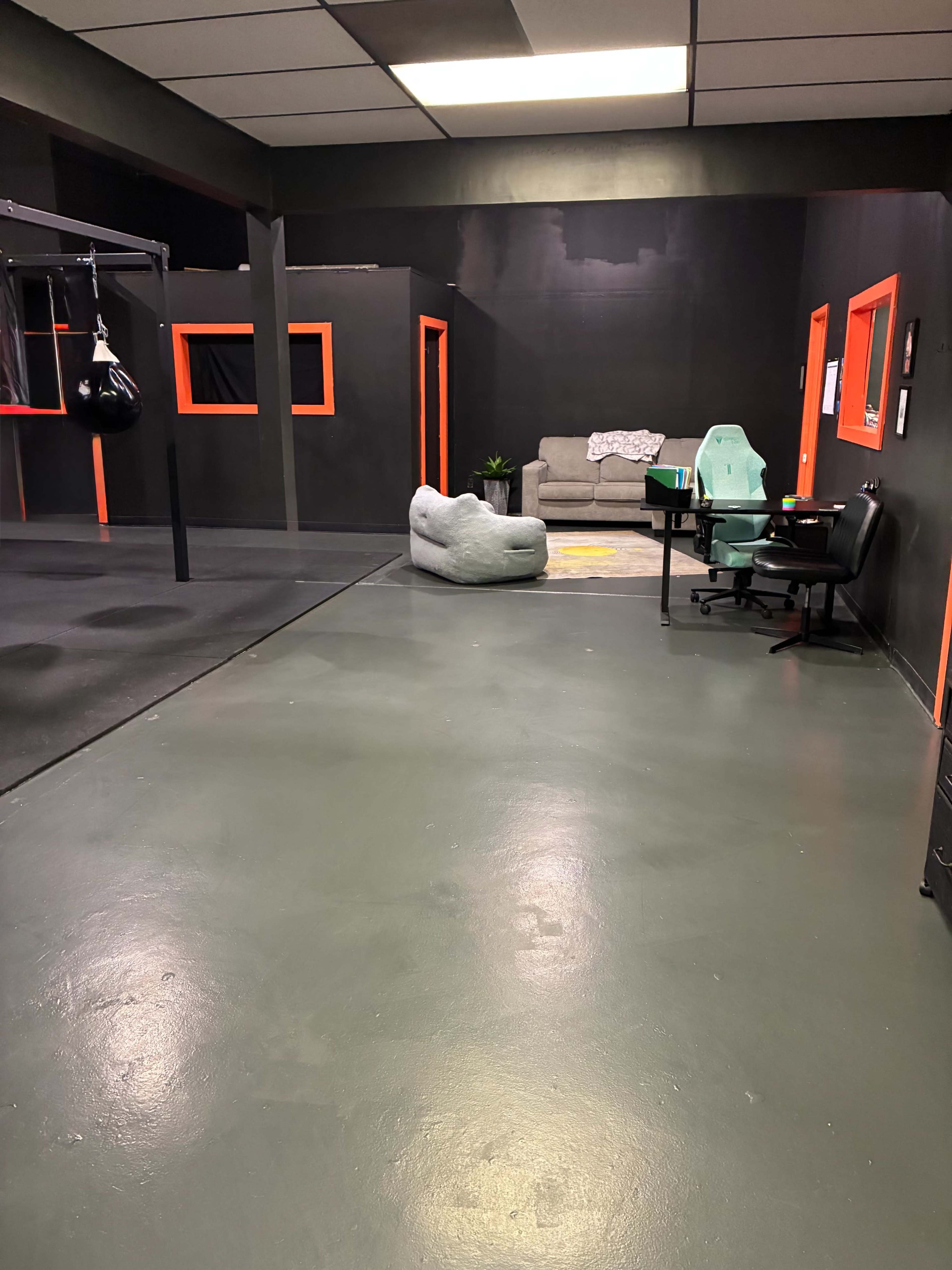 The image shows a room with dark walls, an exercise area featuring a punching bag, and a small seating area with a couch and chairs.