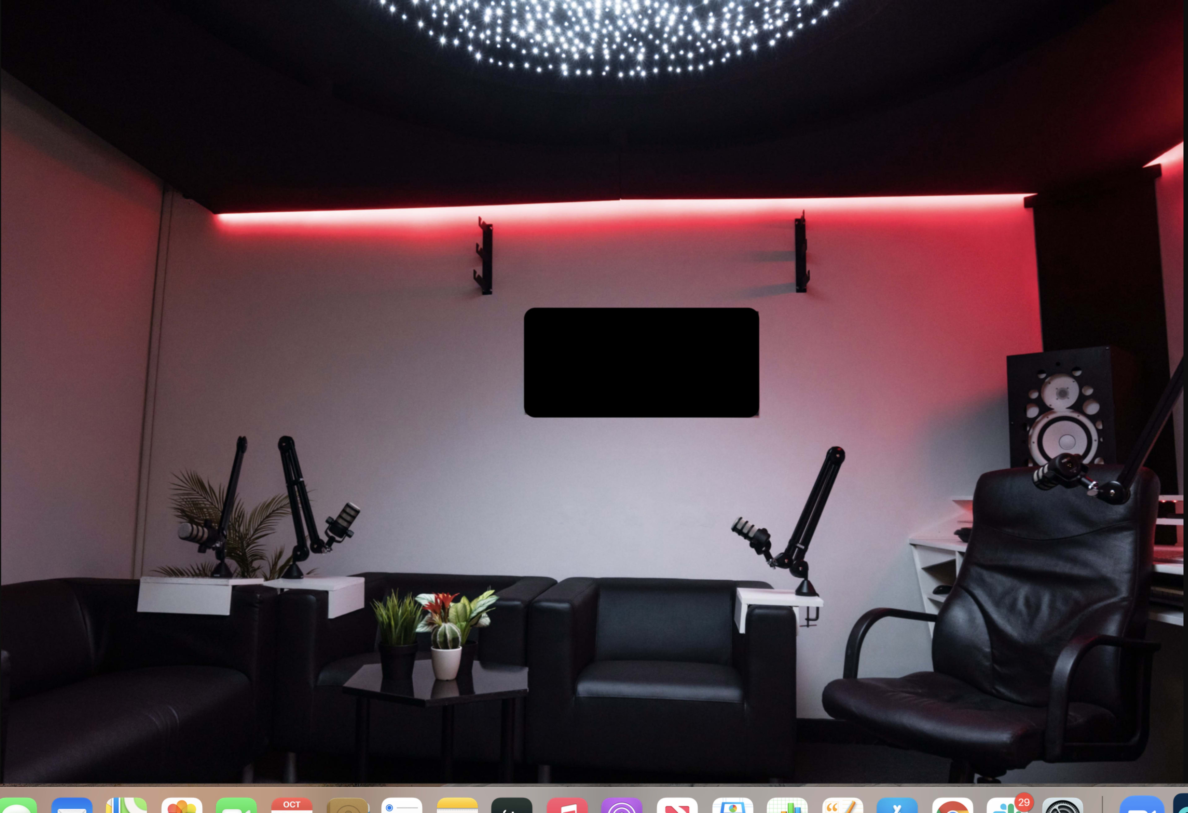 A modern recording studio with black leather chairs, a small table with decorative plants, and sound equipment in a dimly lit space.