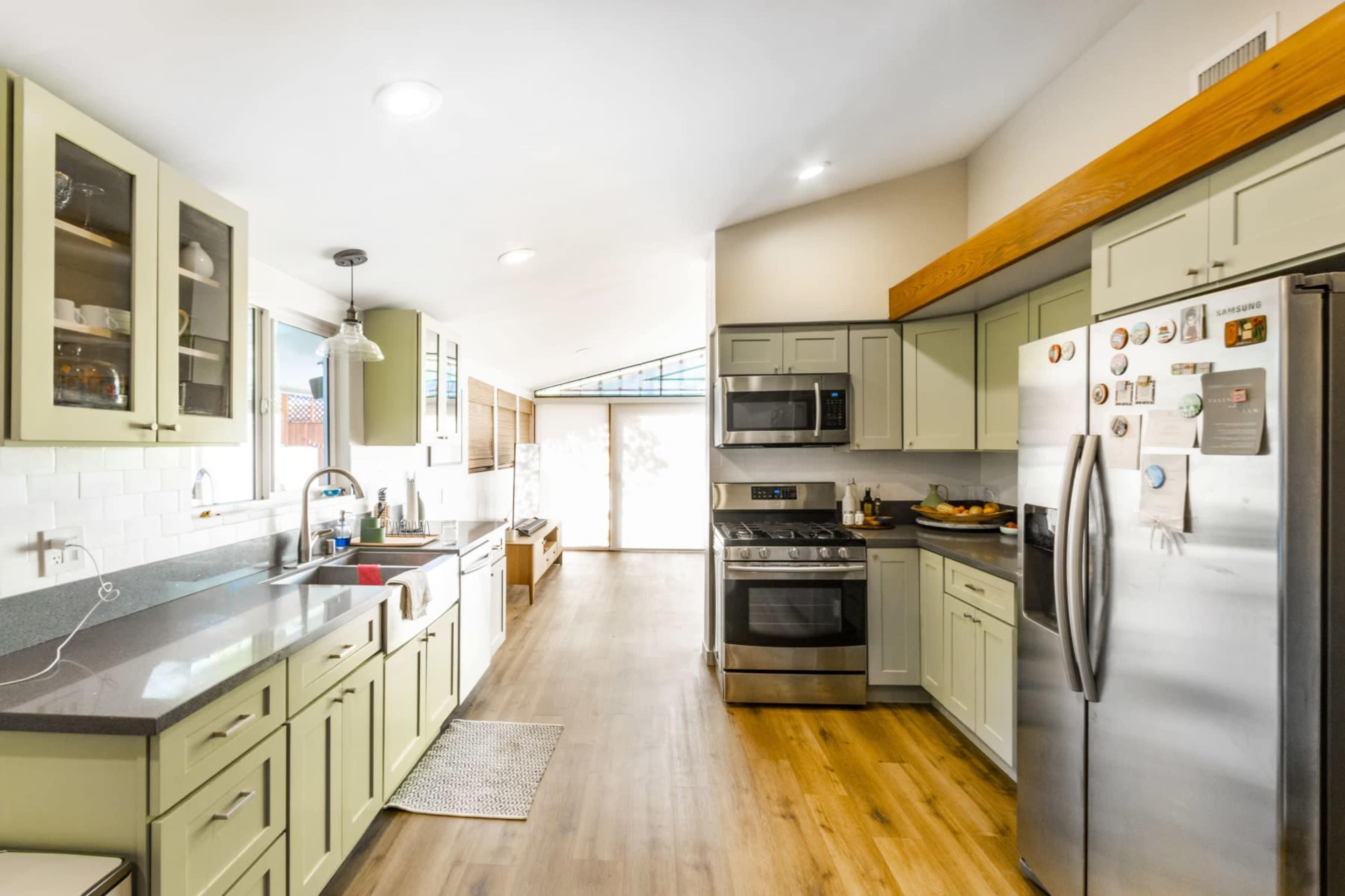 The kitchen features green cabinetry, stainless steel appliances, a gray countertop, and ample natural light from a rear window.