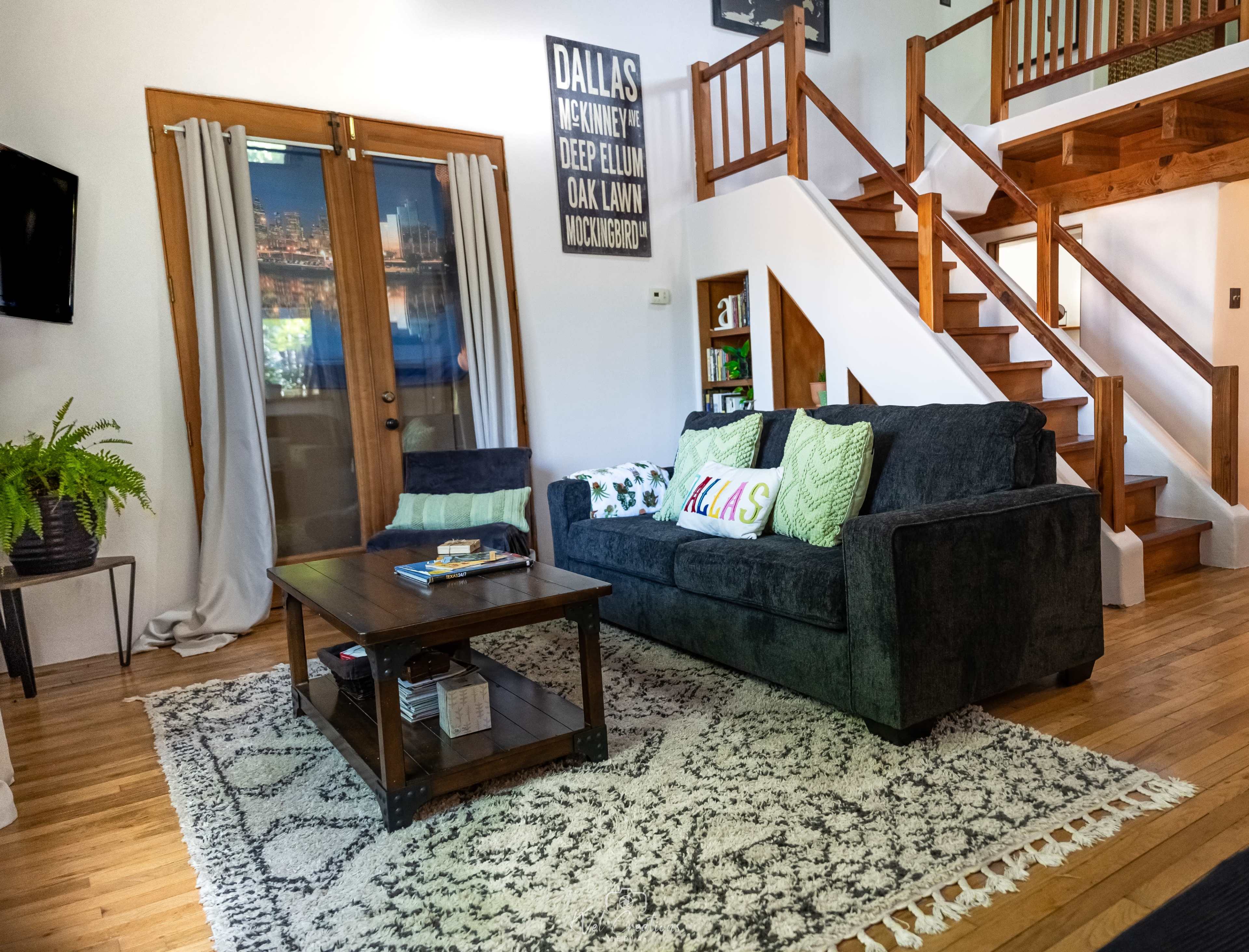 The living room features a dark blue couch with decorative pillows, a wooden coffee table, a patterned area rug, and a staircase leading to an upper level.