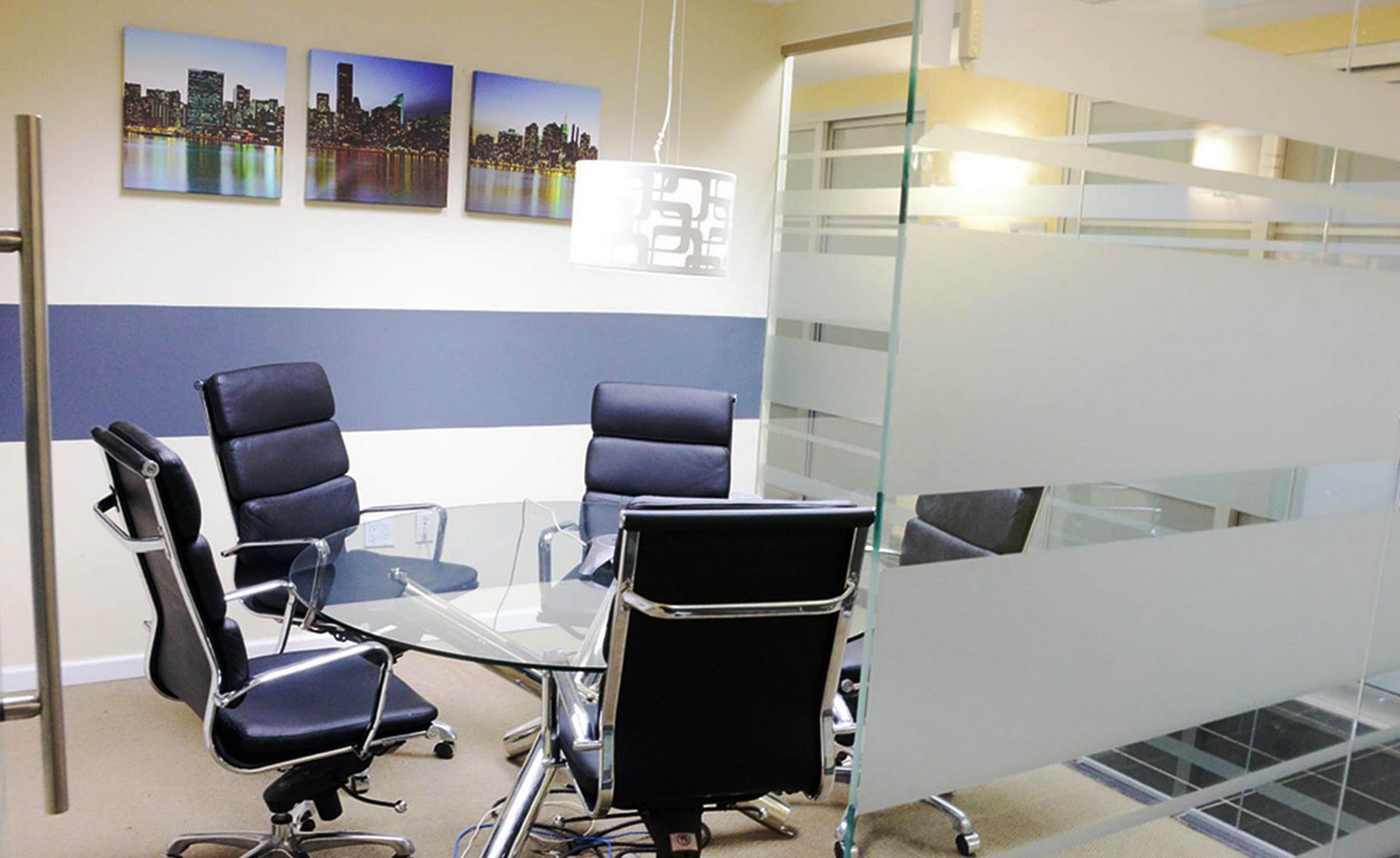 A modern conference room with a glass table, black leather chairs, and cityscape artwork on the walls.