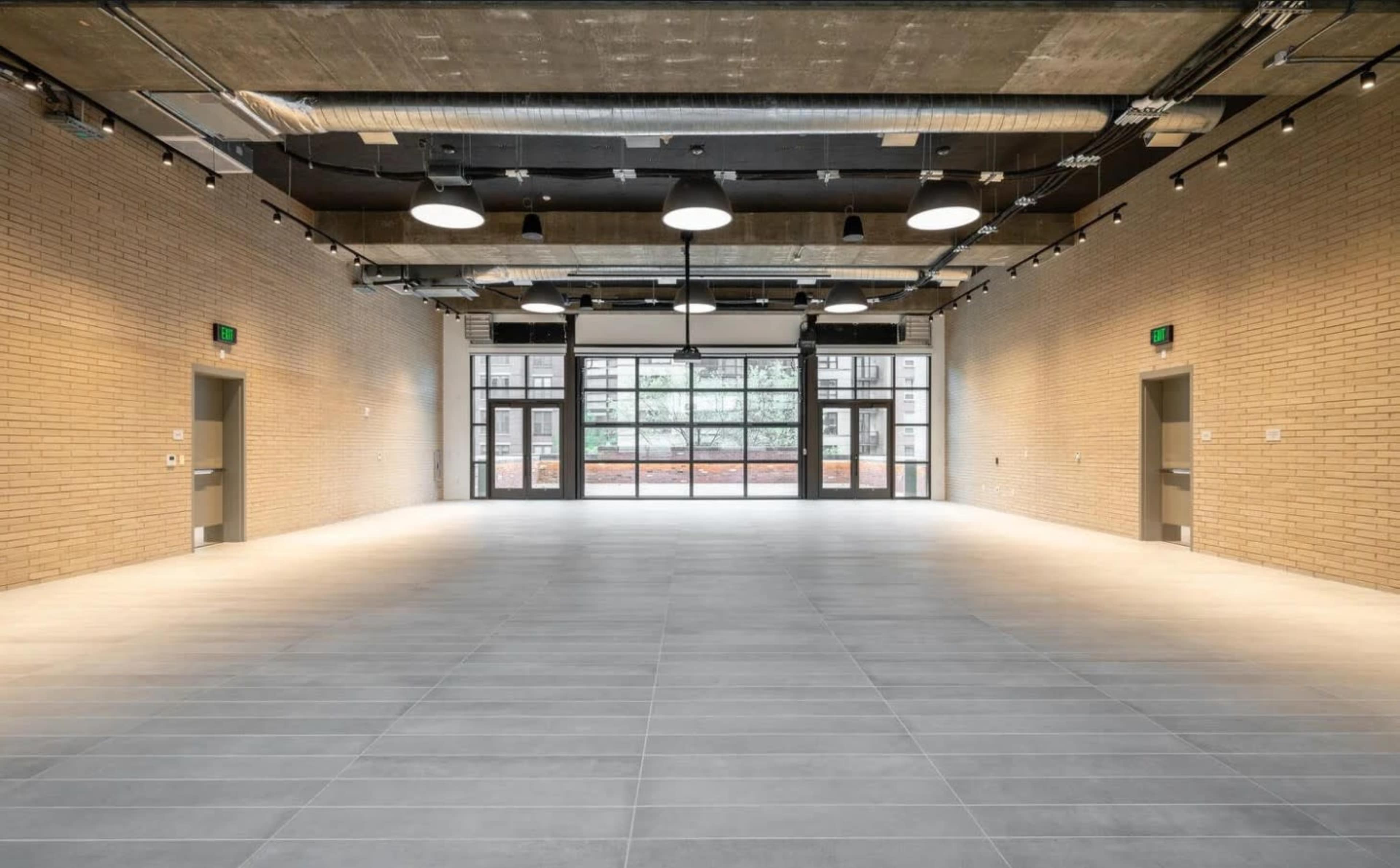 The image shows a spacious, modern interior with light-colored brick walls, large windows, and a tiled floor.