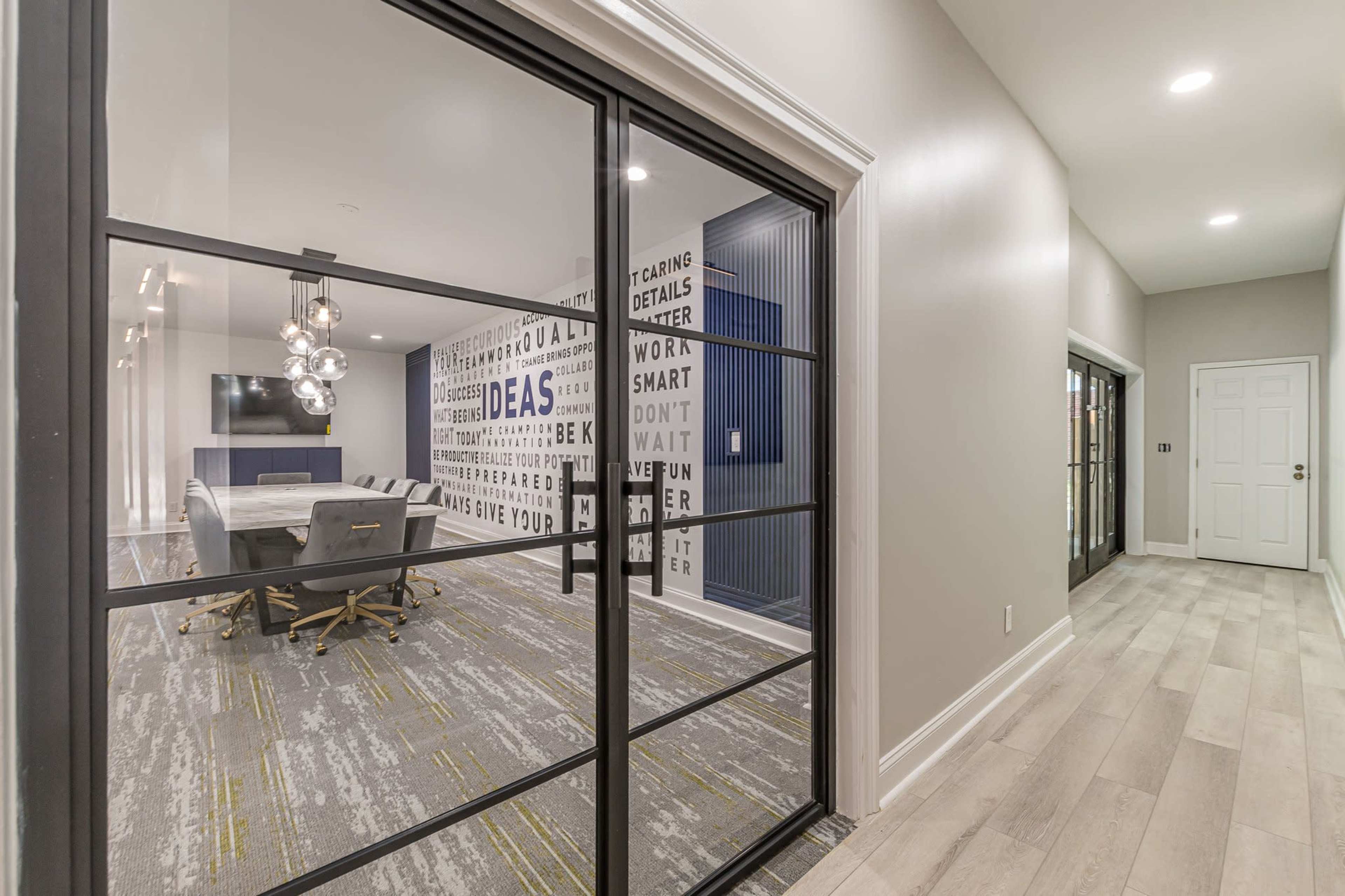 A modern office space with a glass partition, featuring a conference table and walls decorated with motivational words.