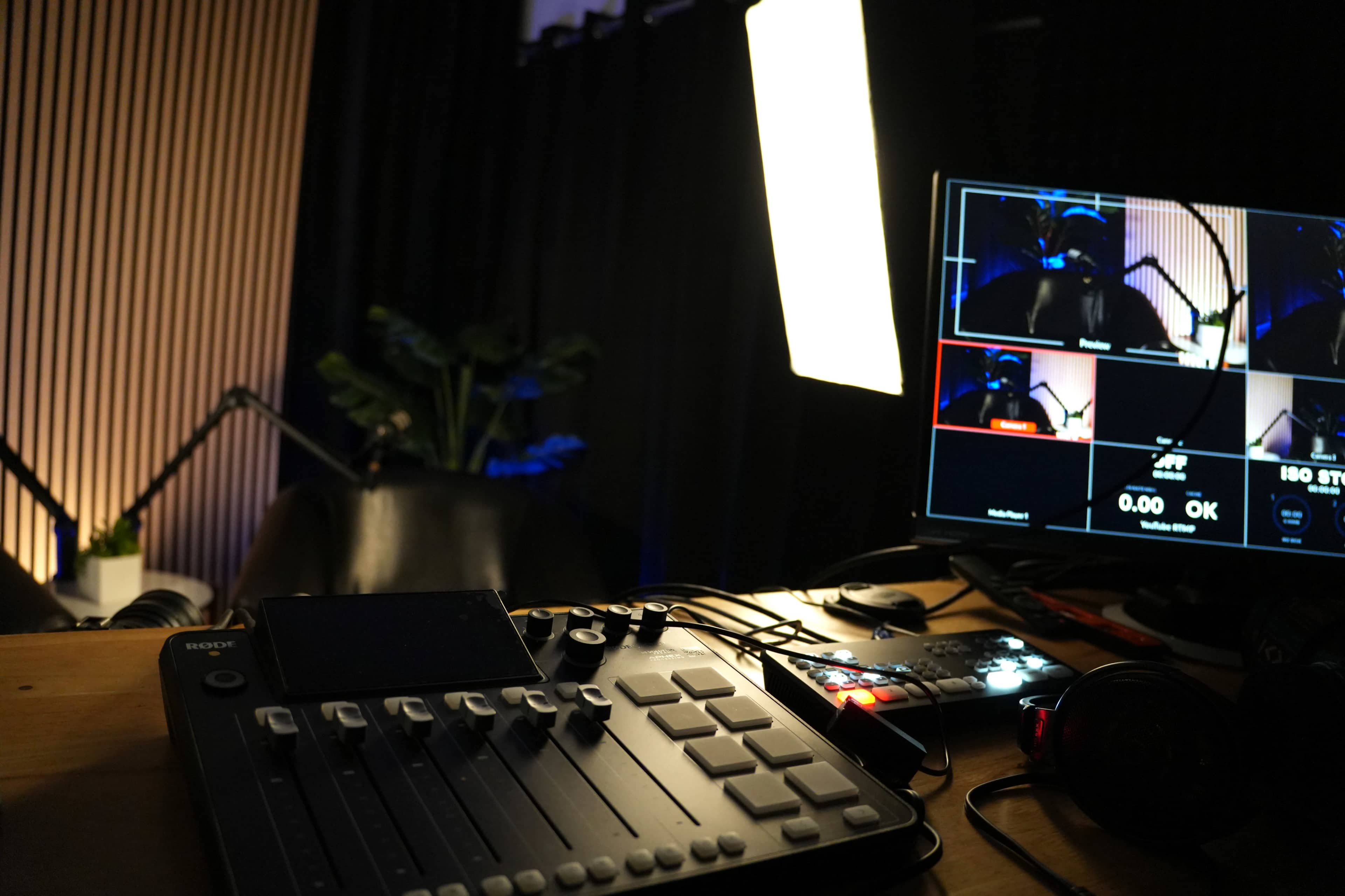 The image shows a recording studio setup with a control panel, multiple screens displaying video feeds, and a bright light illuminating the space.