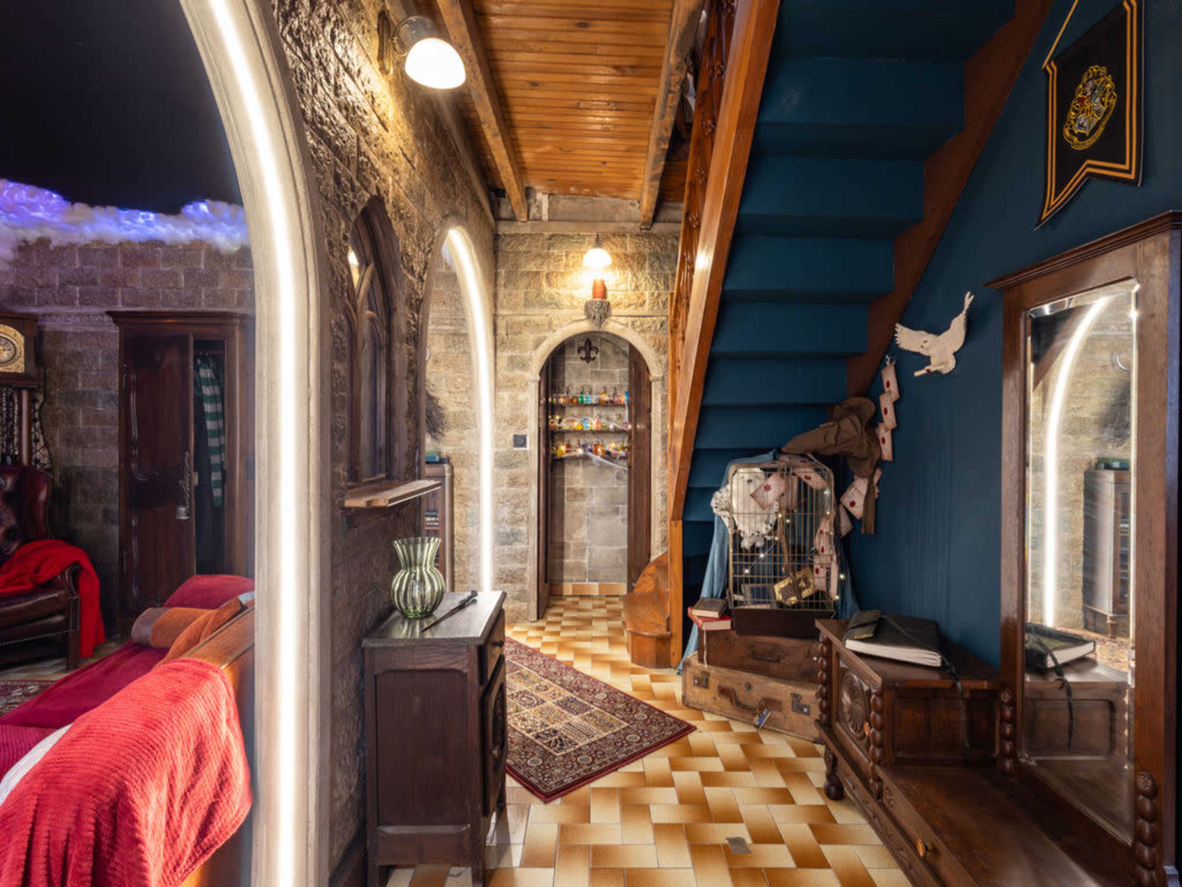 The image shows a hallway with stone walls, a staircase leading to a second level, a wooden mirror, and a patterned floor.