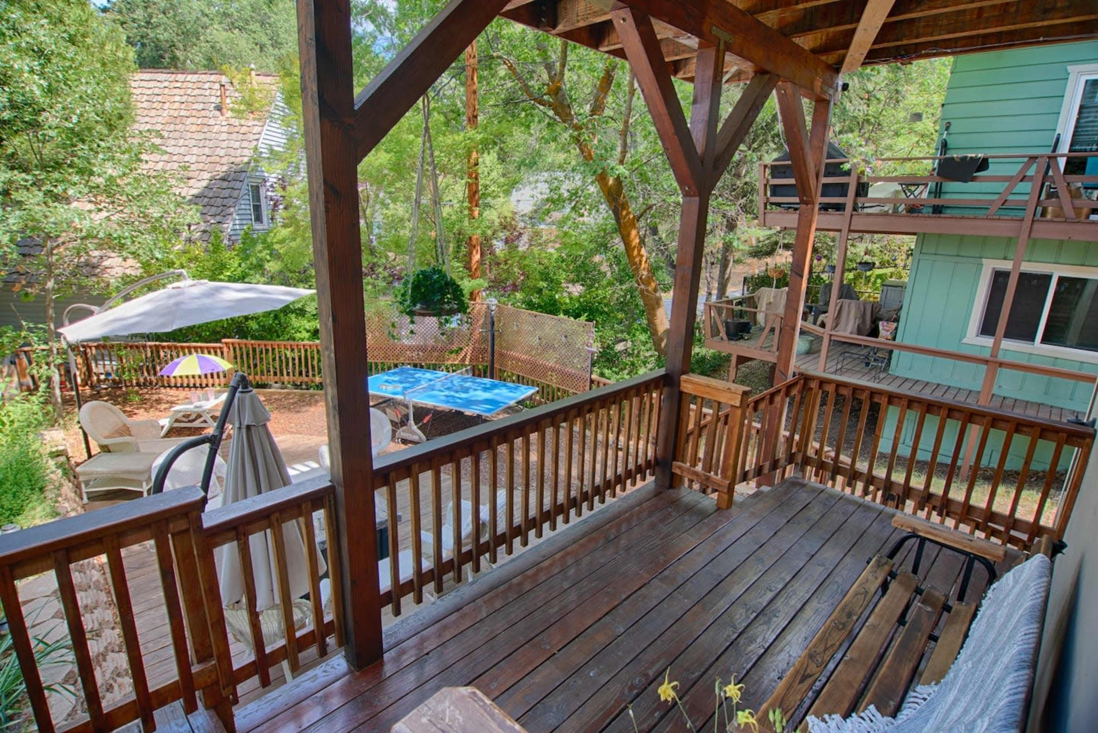 The image shows a wooden deck overlooking a backyard with outdoor furniture, a patio umbrella, and a blue pool.