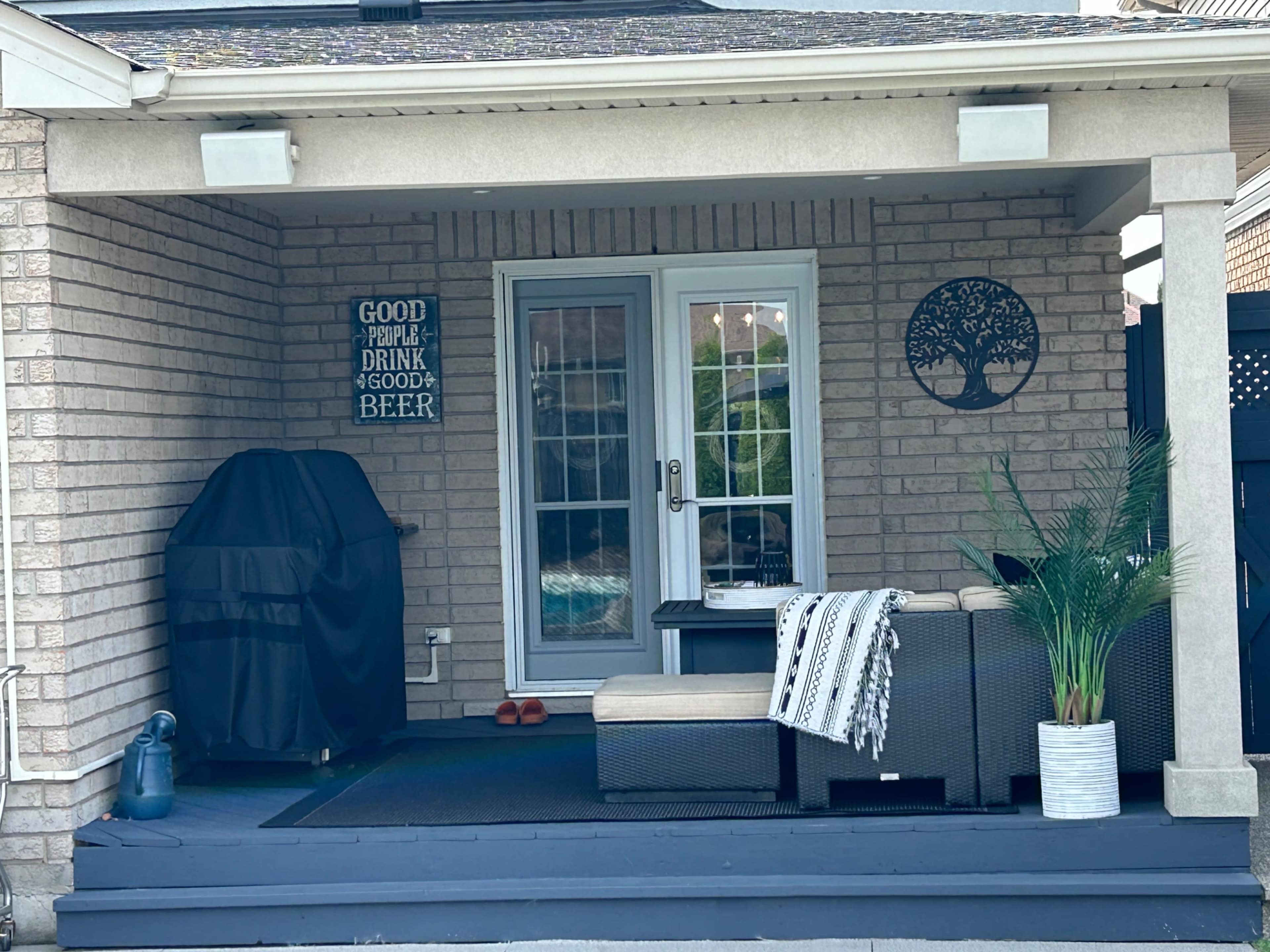 A covered porch with a grill, outdoor seating area, and a sign that reads "Good people drink good beer."