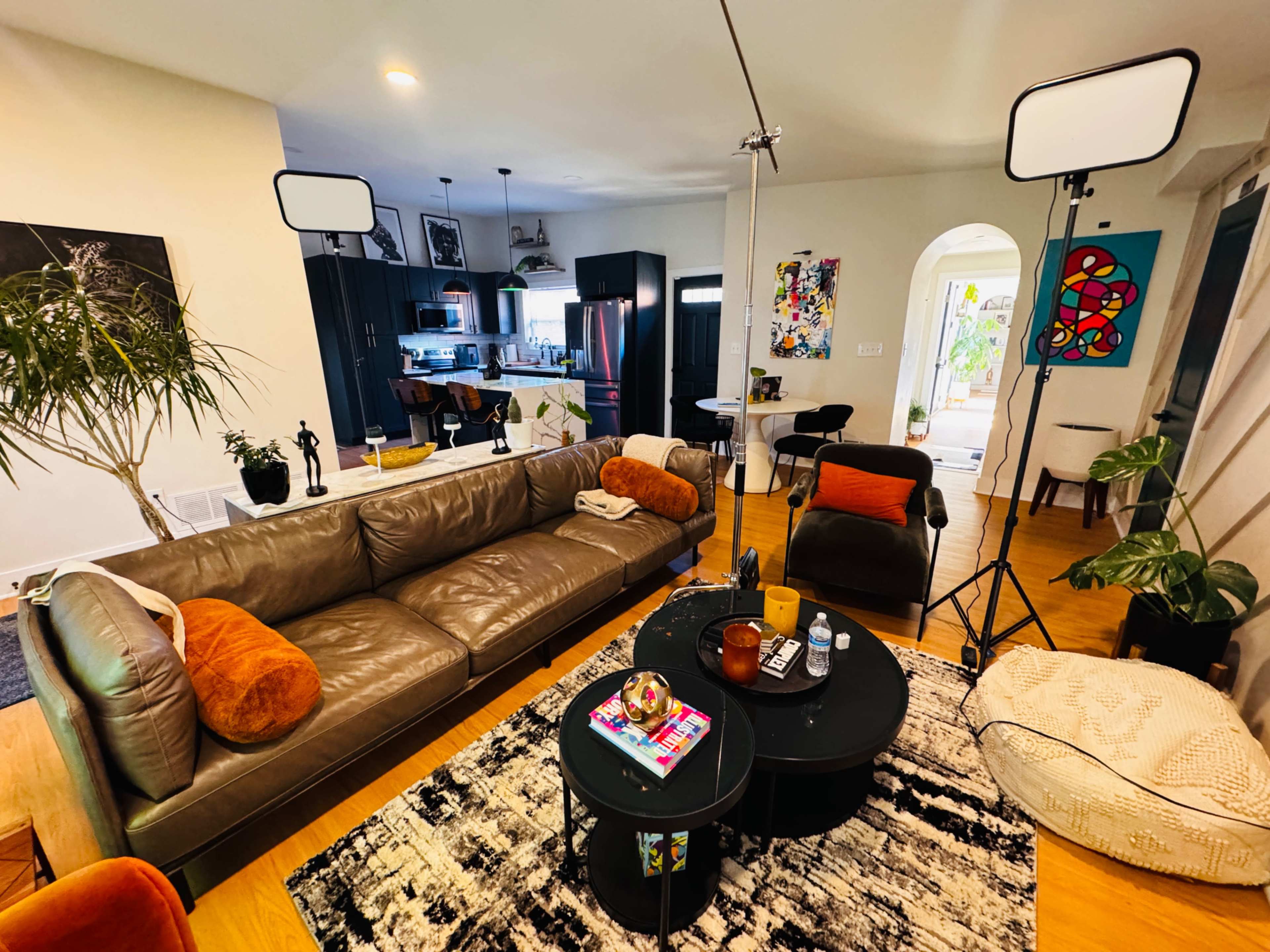 The image shows a modern living room with a brown leather sofa, a black circular coffee table, and a backdrop of a kitchen area with contemporary decor.