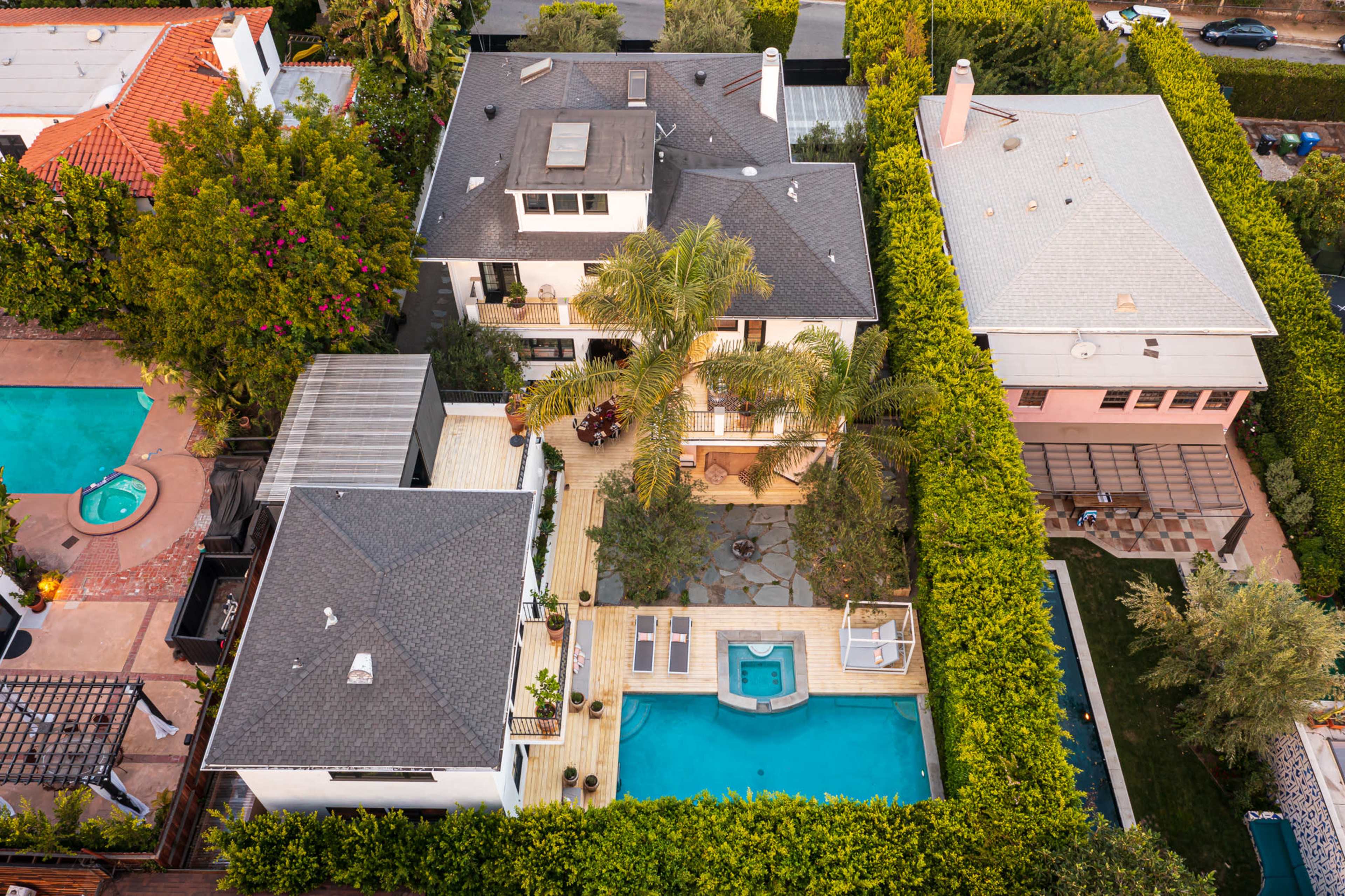 The image shows an aerial view of several homes with swimming pools surrounded by greenery in a residential neighborhood.