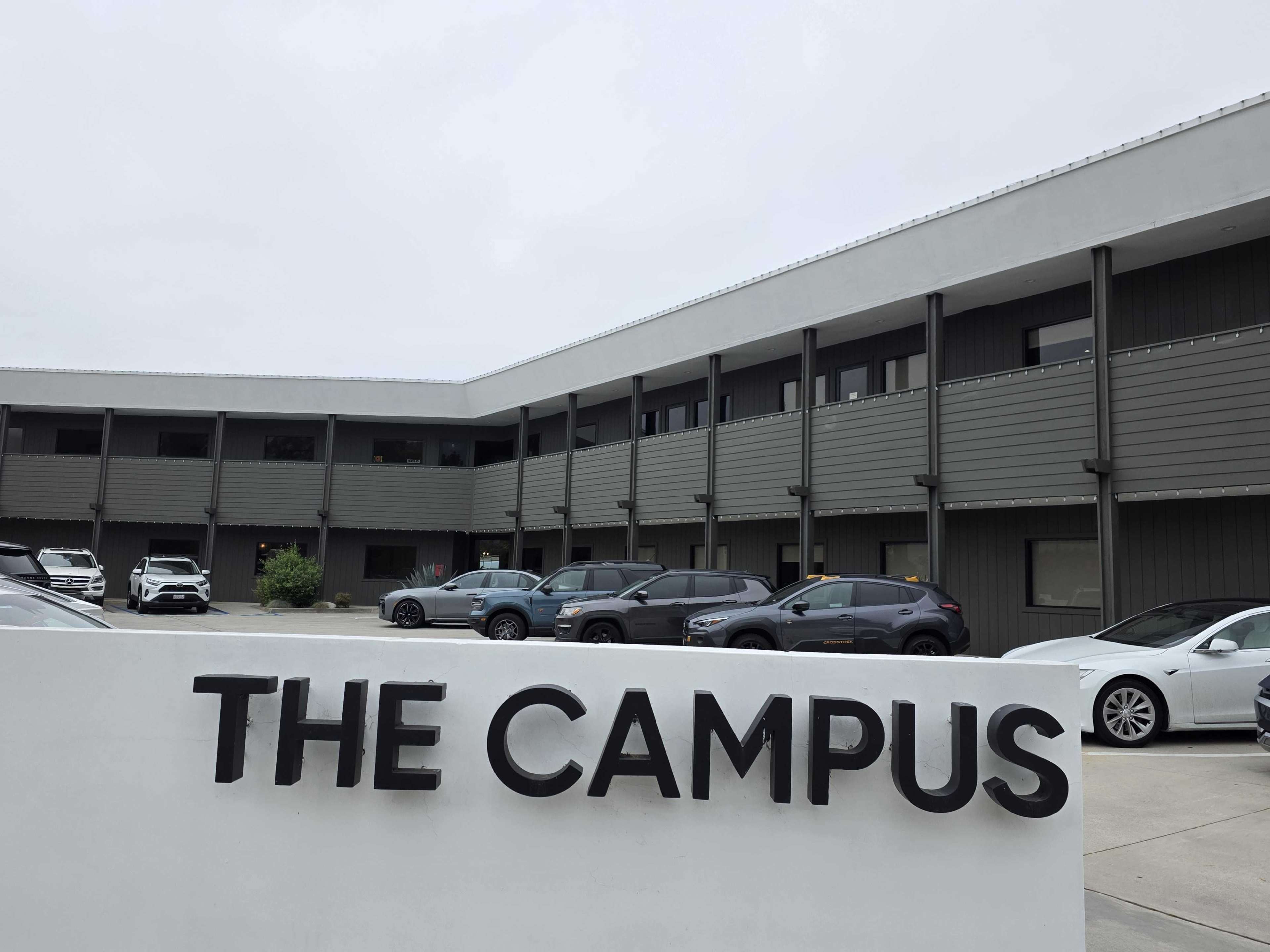 The image shows a modern building complex labeled "THE CAMPUS," with multiple parked cars in front of it.