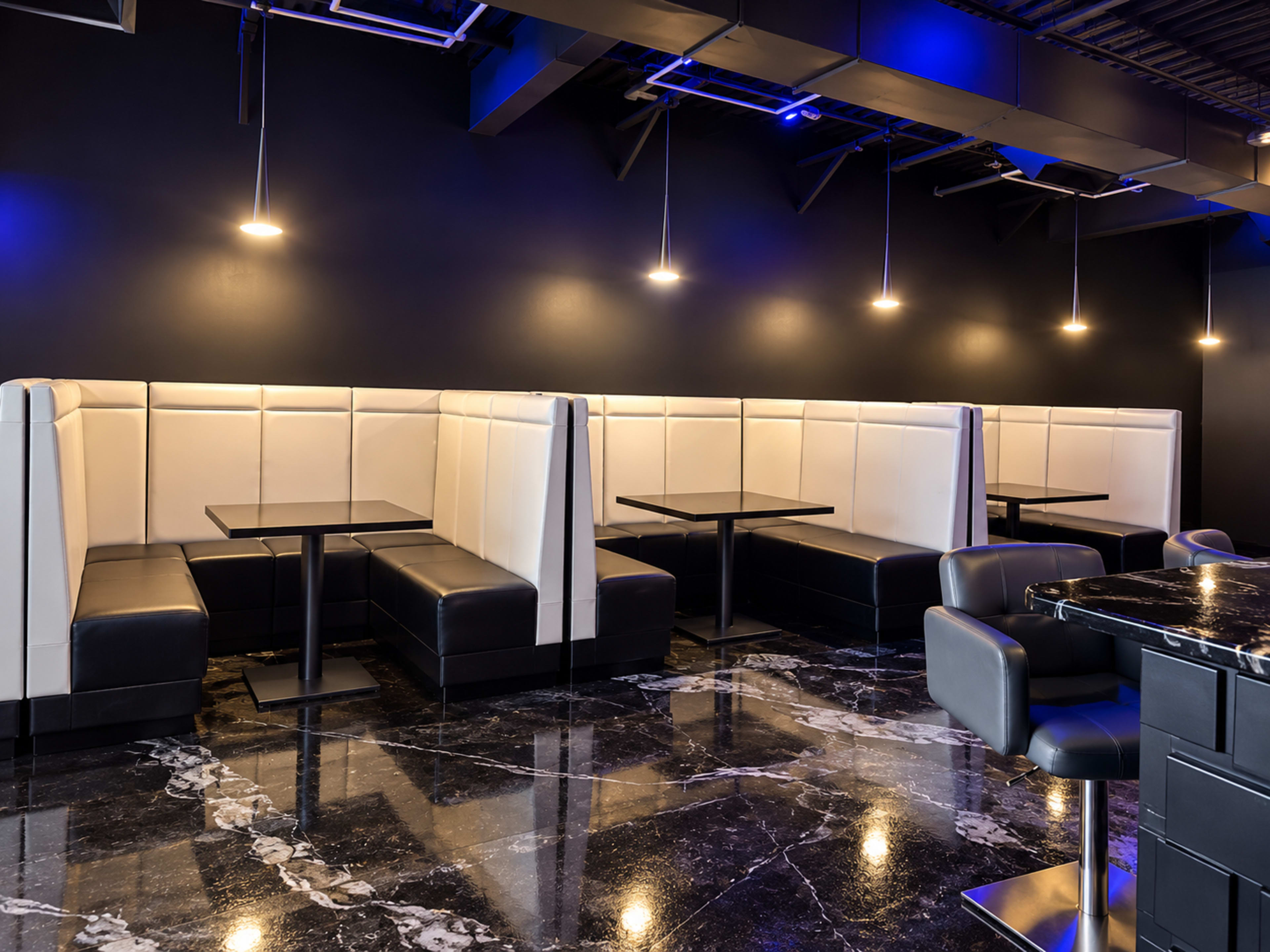 The image shows a modern restaurant interior featuring black and white booth seating with dark marble flooring and dim overhead lighting.