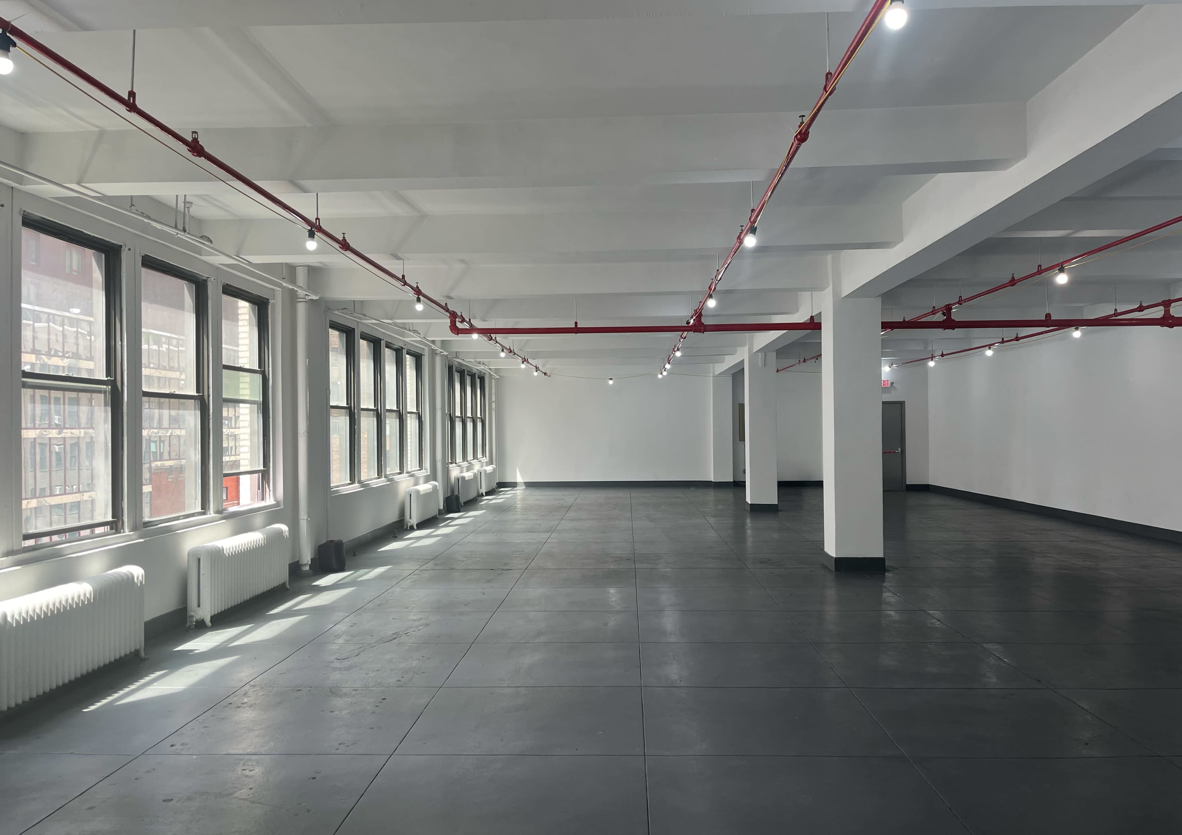 The image shows an empty, well-lit industrial space with large windows and concrete flooring.