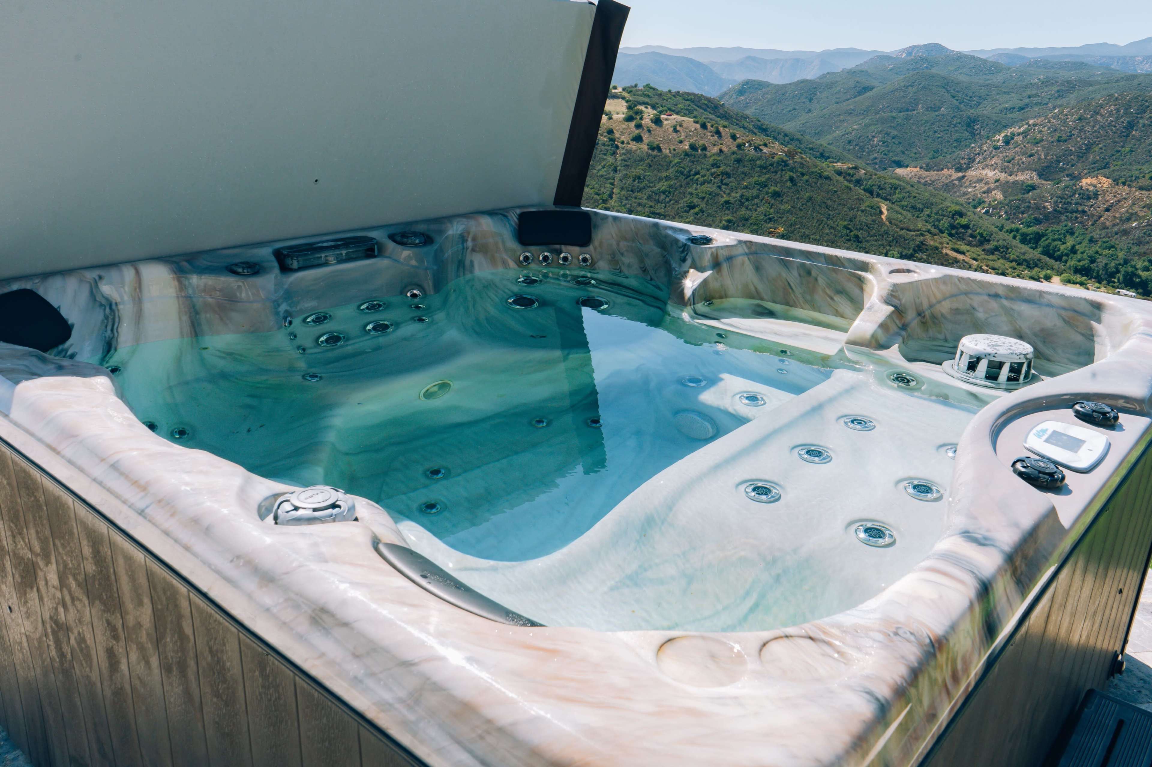 A hot tub filled with water sits on a deck overlooking rolling hills and mountains.