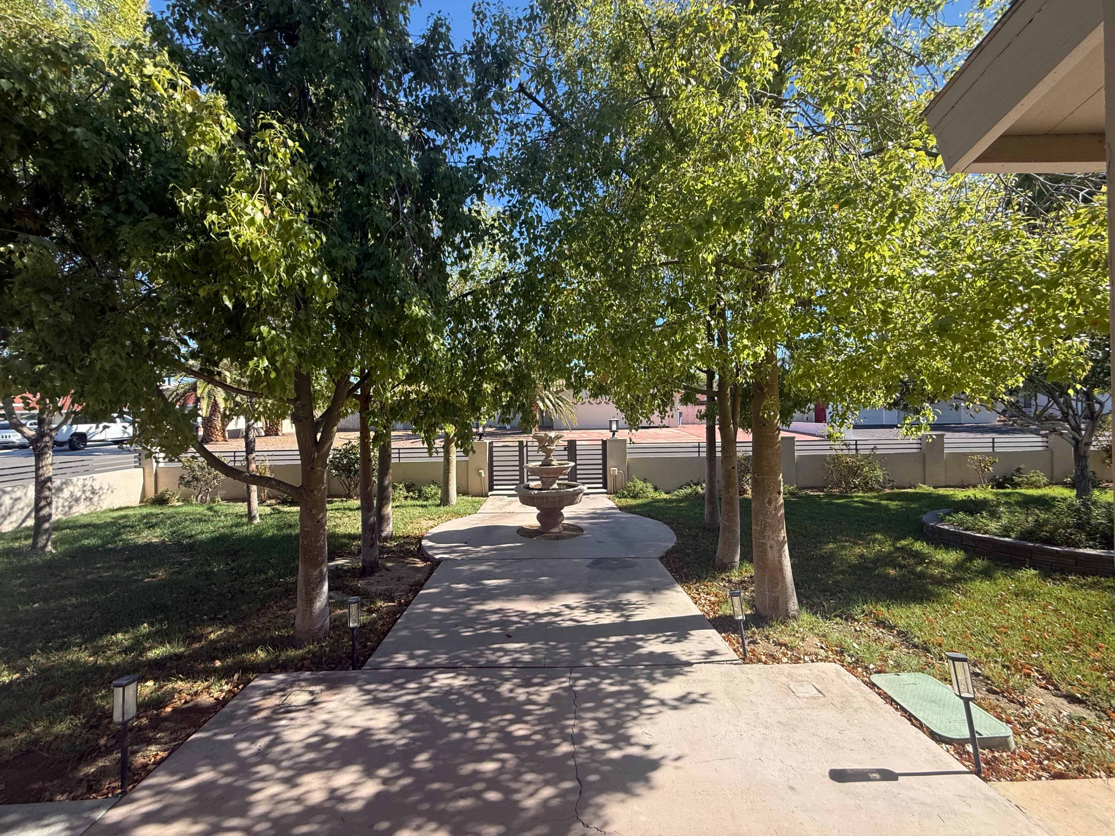The image shows a pathway lined with trees leading to a fountain in a landscaped yard.