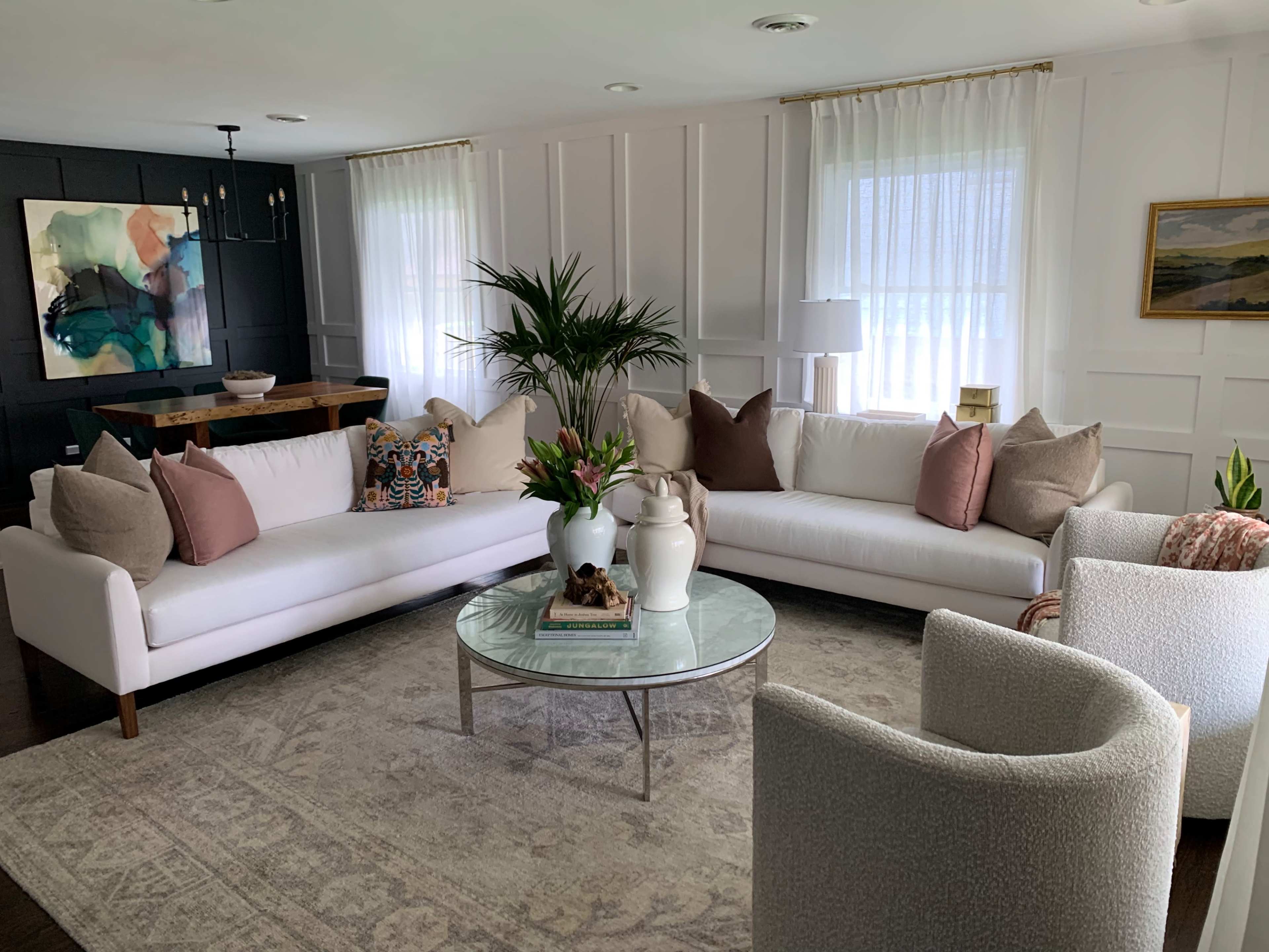 The living room features a large U-shaped sectional sofa with decorative pillows, a coffee table in the center, and large windows allowing natural light.