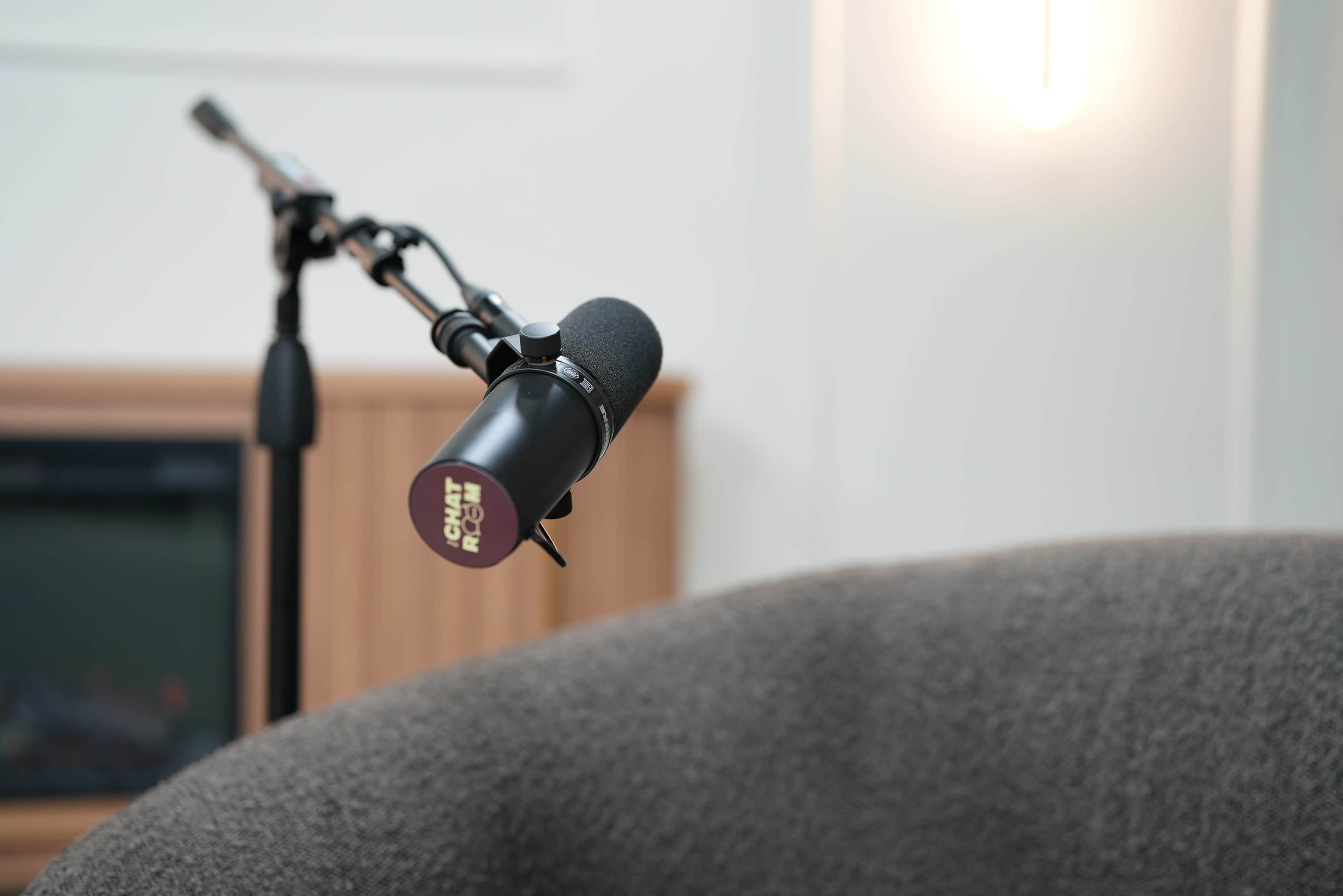 The image features a close-up of a microphone mounted on a stand, positioned near a soft gray couch in a well-lit room.