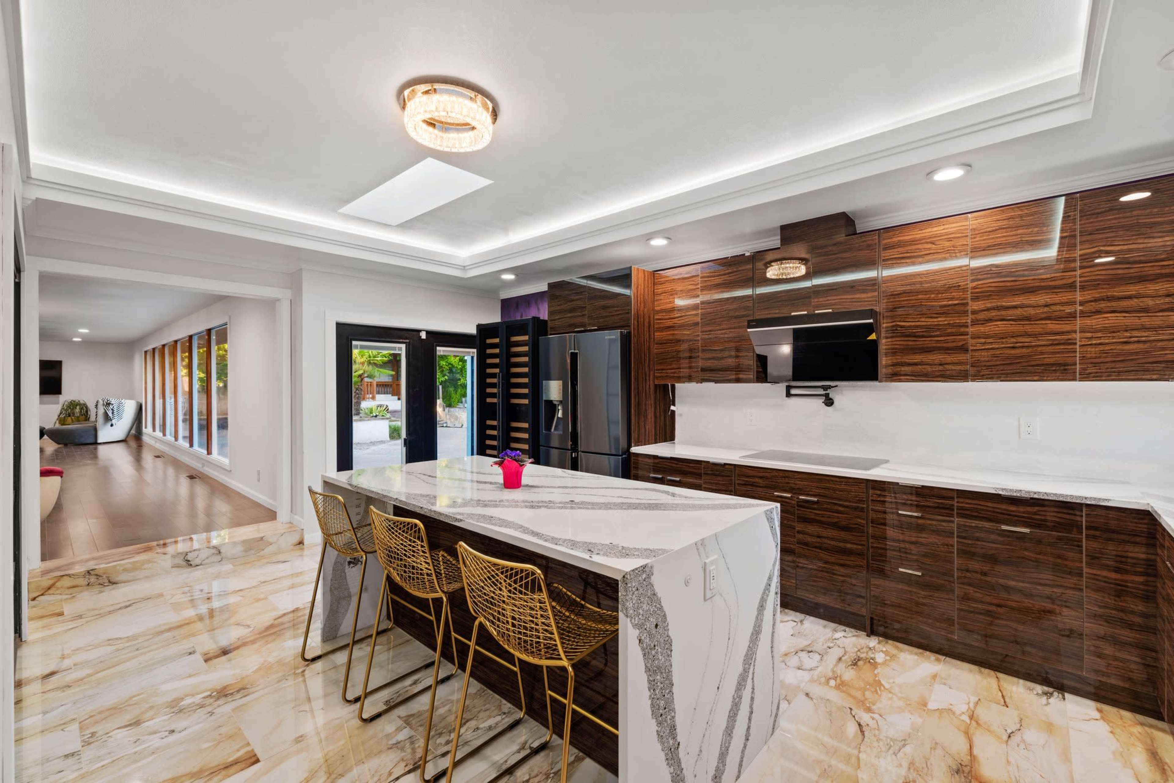 A modern kitchen with dark wood cabinetry, a large white marble island, and gold bar stools.