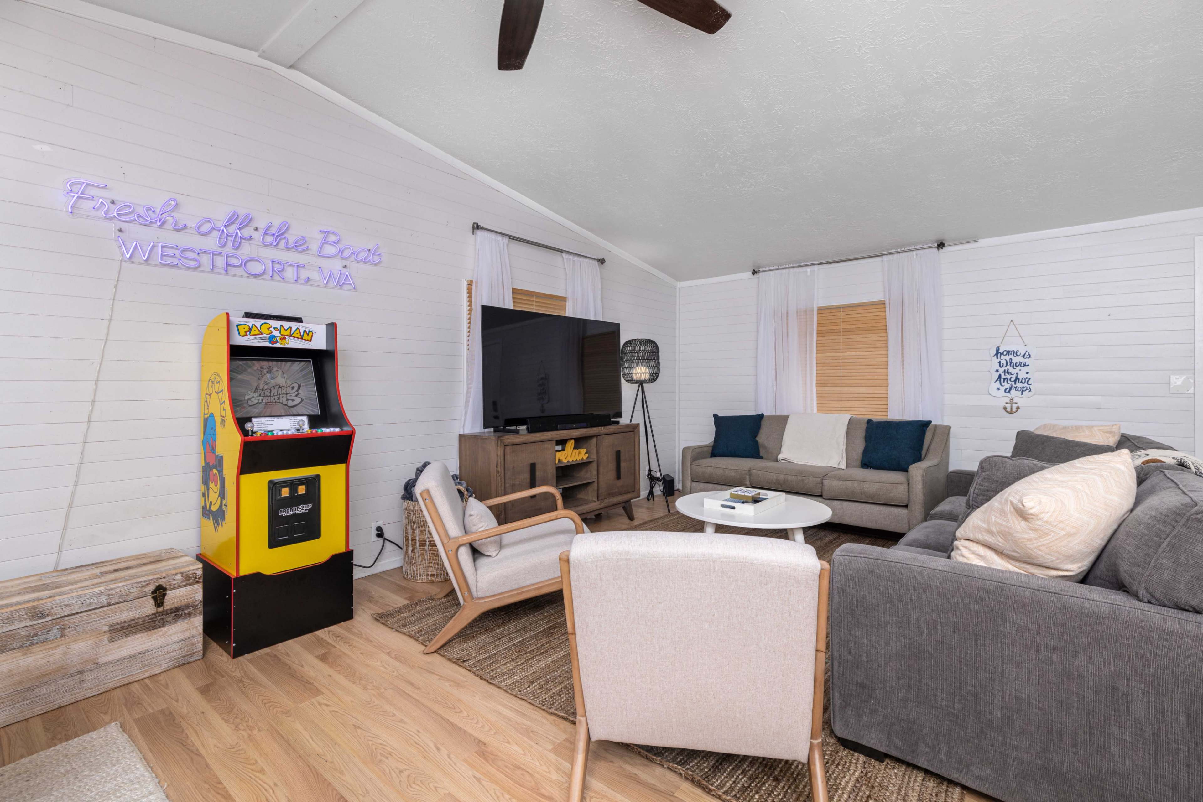 The living room features a mix of modern and vintage decor, including a neon sign, a large television, a retro arcade game machine, and comfortable seating arrangements.