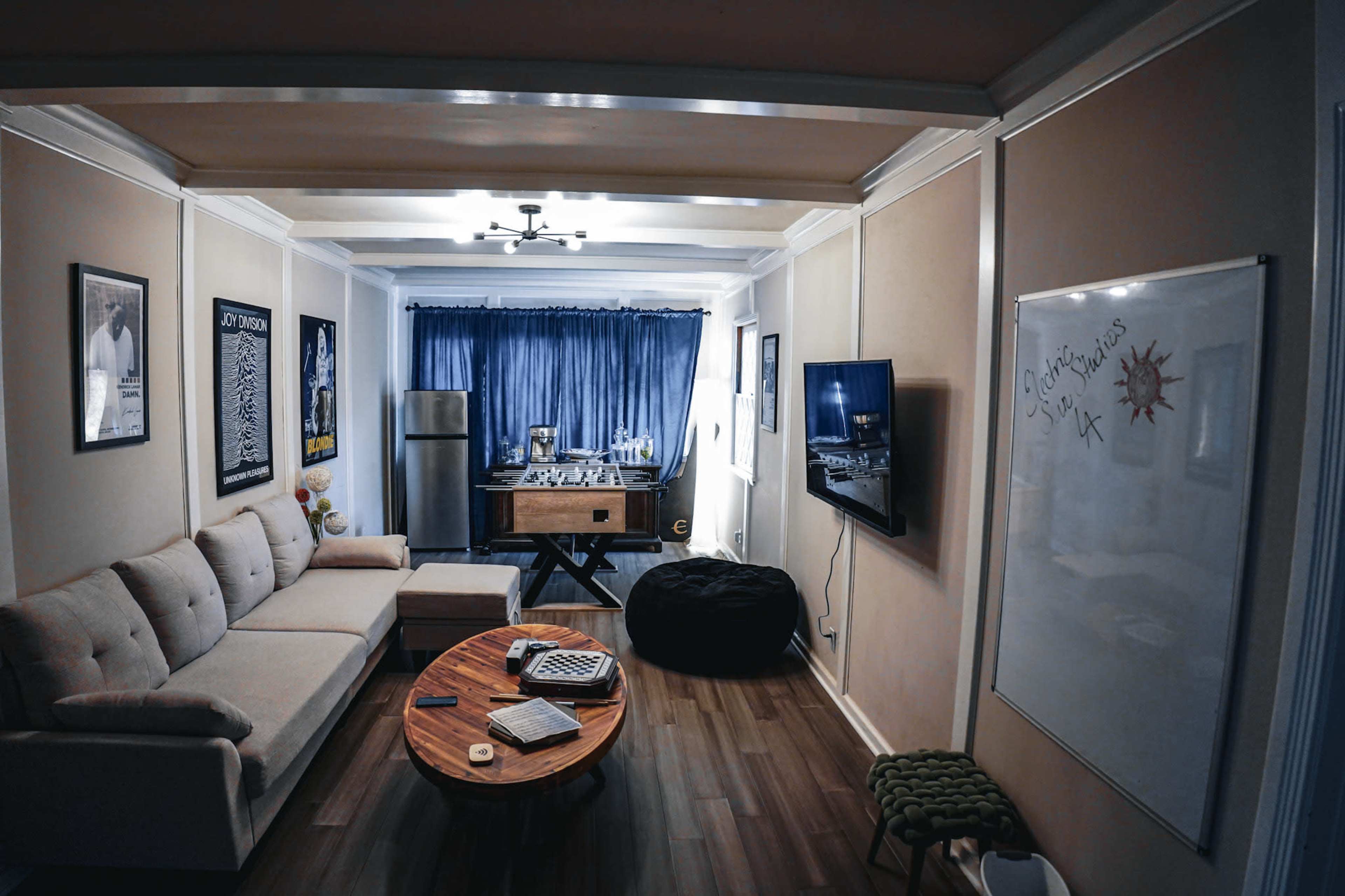 A cozy living room with a beige sectional sofa, a wooden coffee table, and a foosball table in the background.