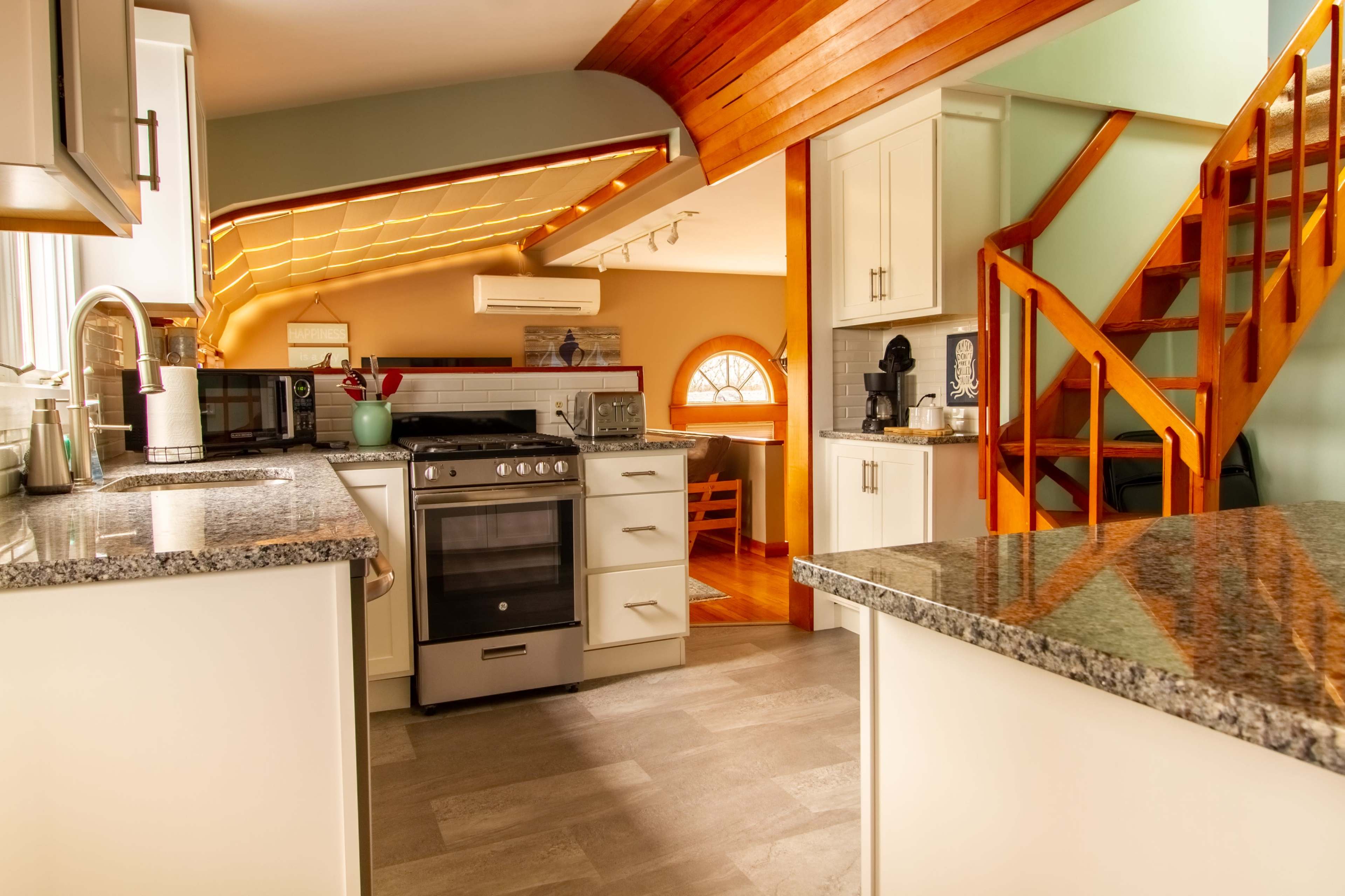 A modern kitchen with granite countertops, white cabinetry, and an open layout that leads to a wooden staircase.