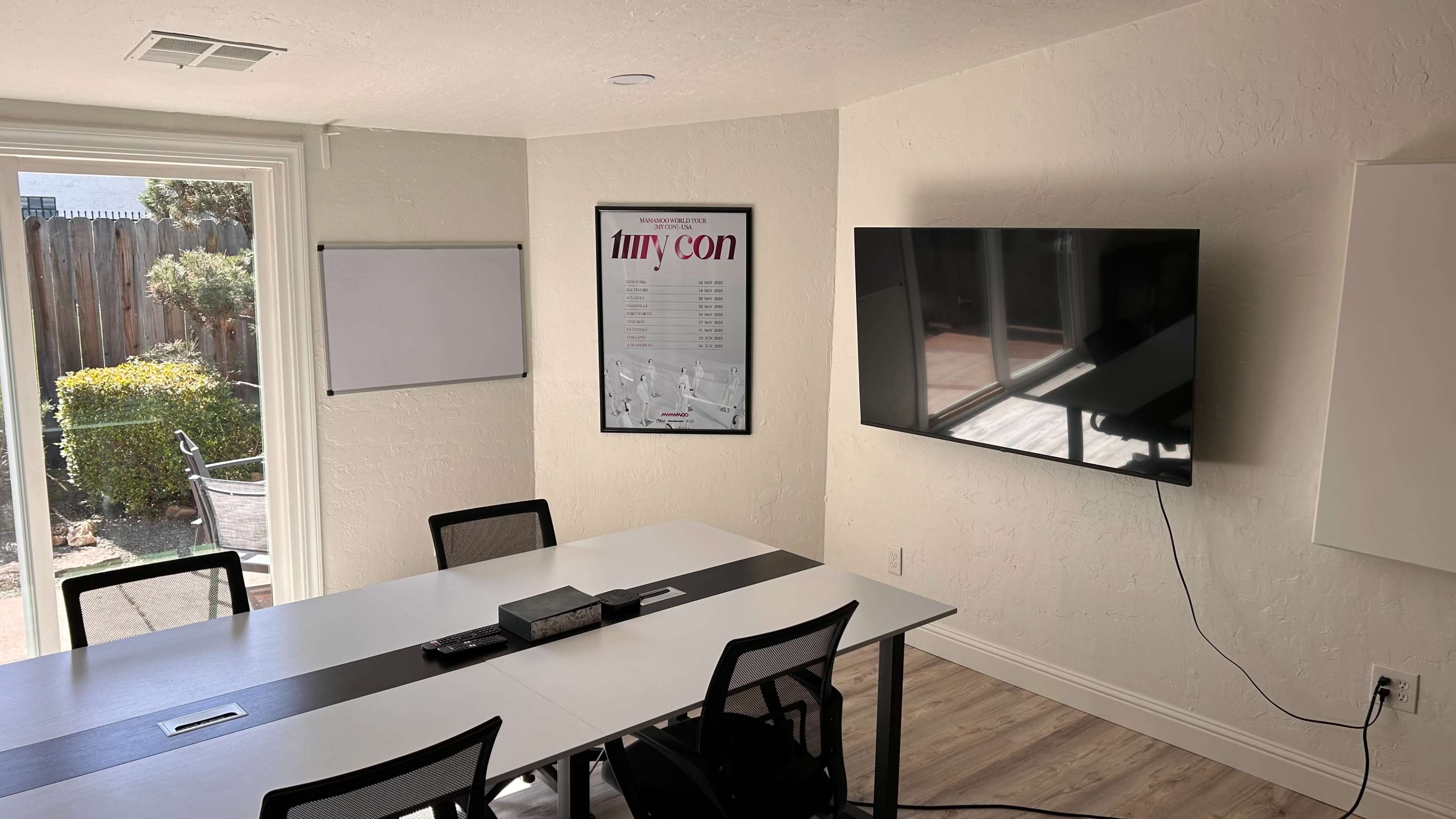 A conference room is equipped with a wall-mounted TV, a whiteboard, and a table surrounded by chairs.