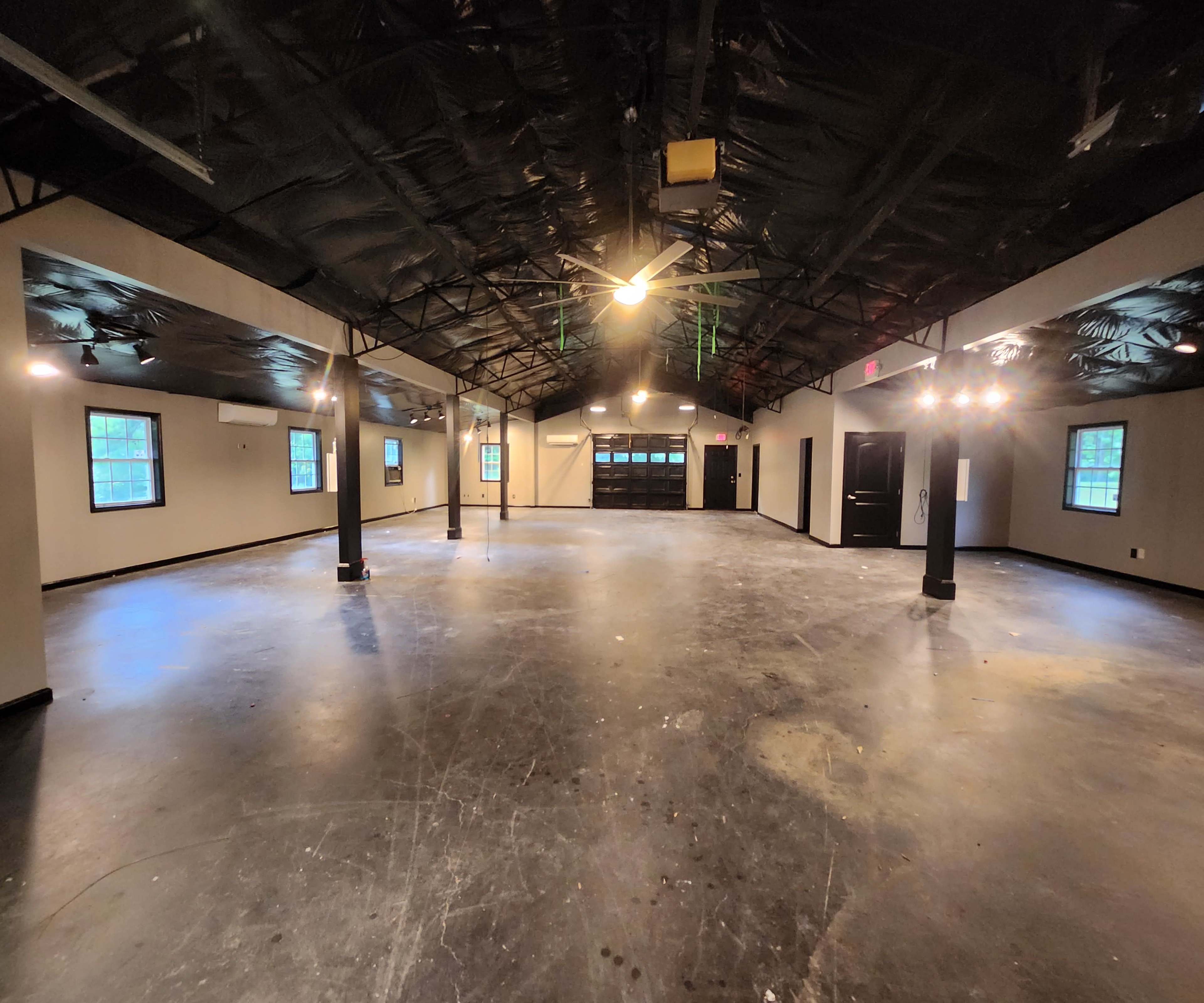 An empty, spacious room with a polished floor, ceiling fans, and multiple windows.