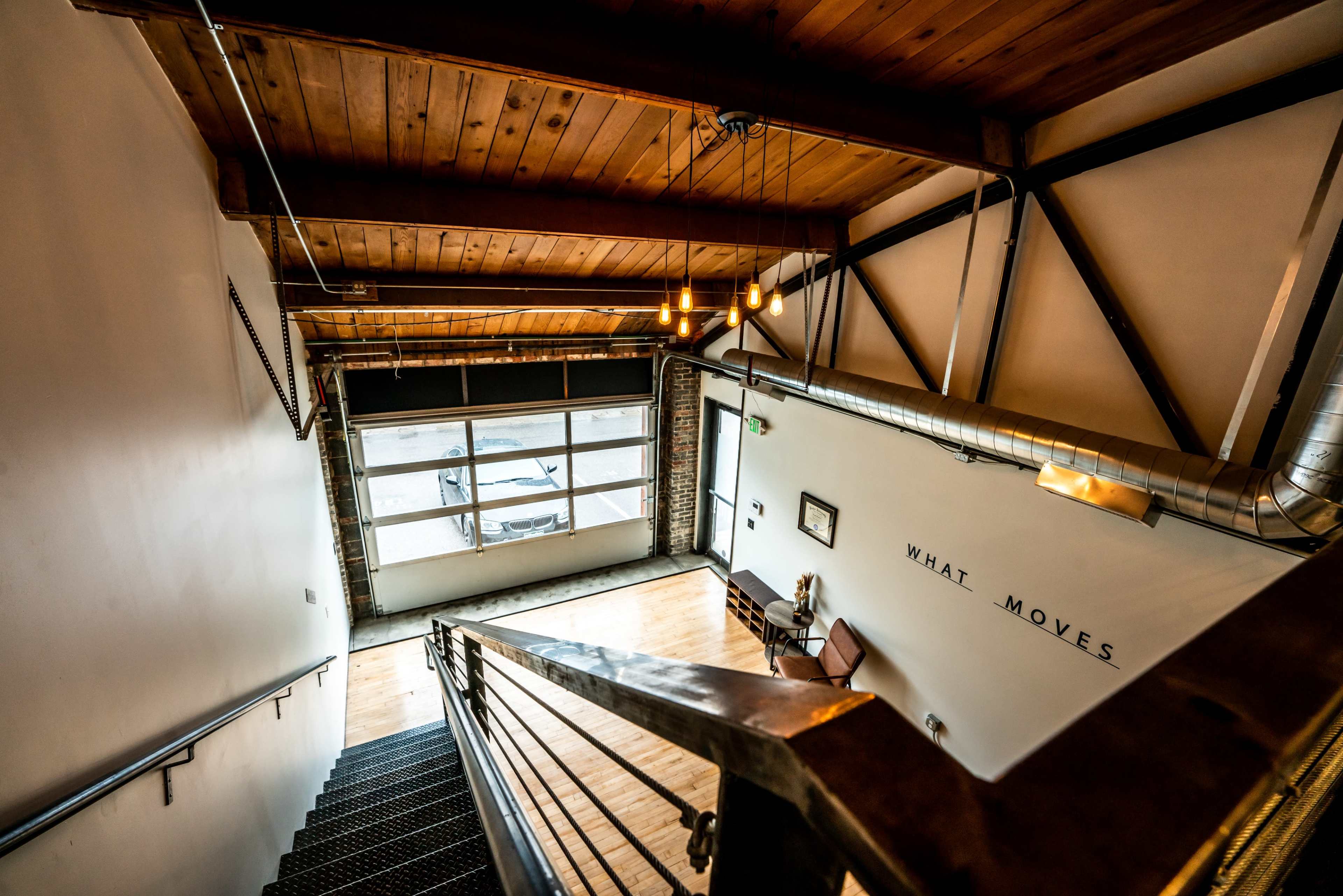 A stairway leading down to a space with large windows, wooden beams, and an industrial-style design.