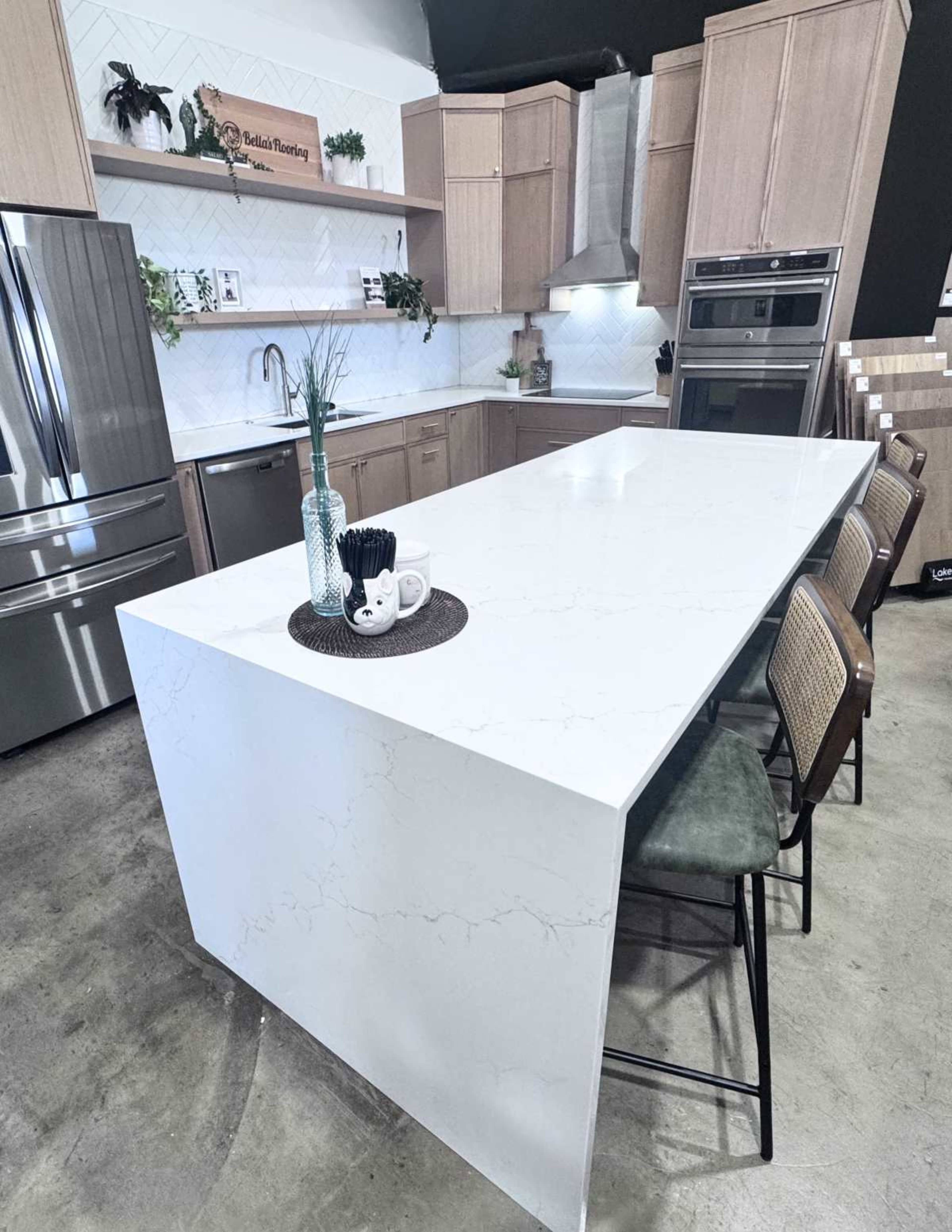 The image shows a modern kitchen featuring a white countertop island, stainless steel appliances, and wooden cabinetry.